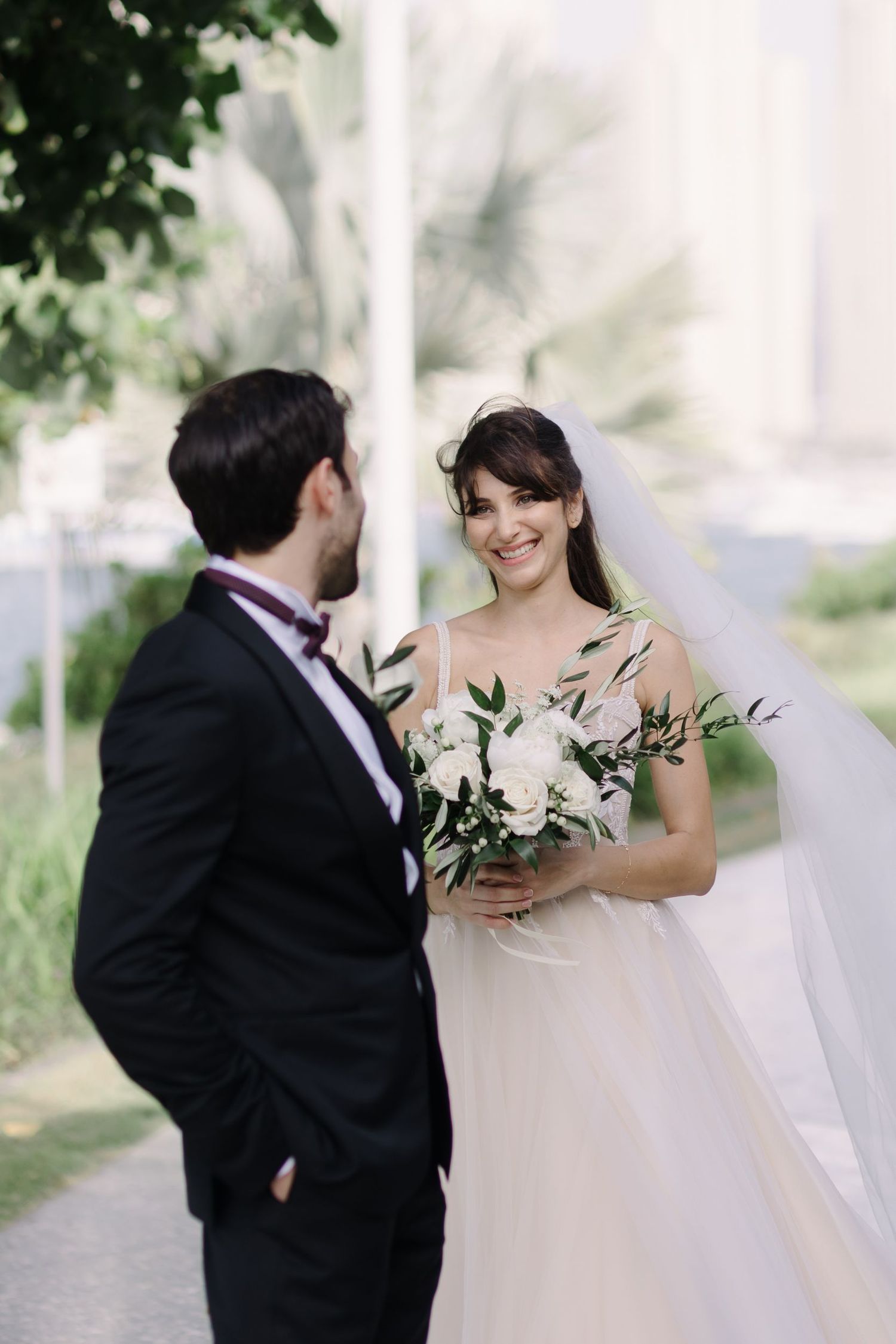 Romantic wedding couple sharing a moment outdoors with greenery and white florals.