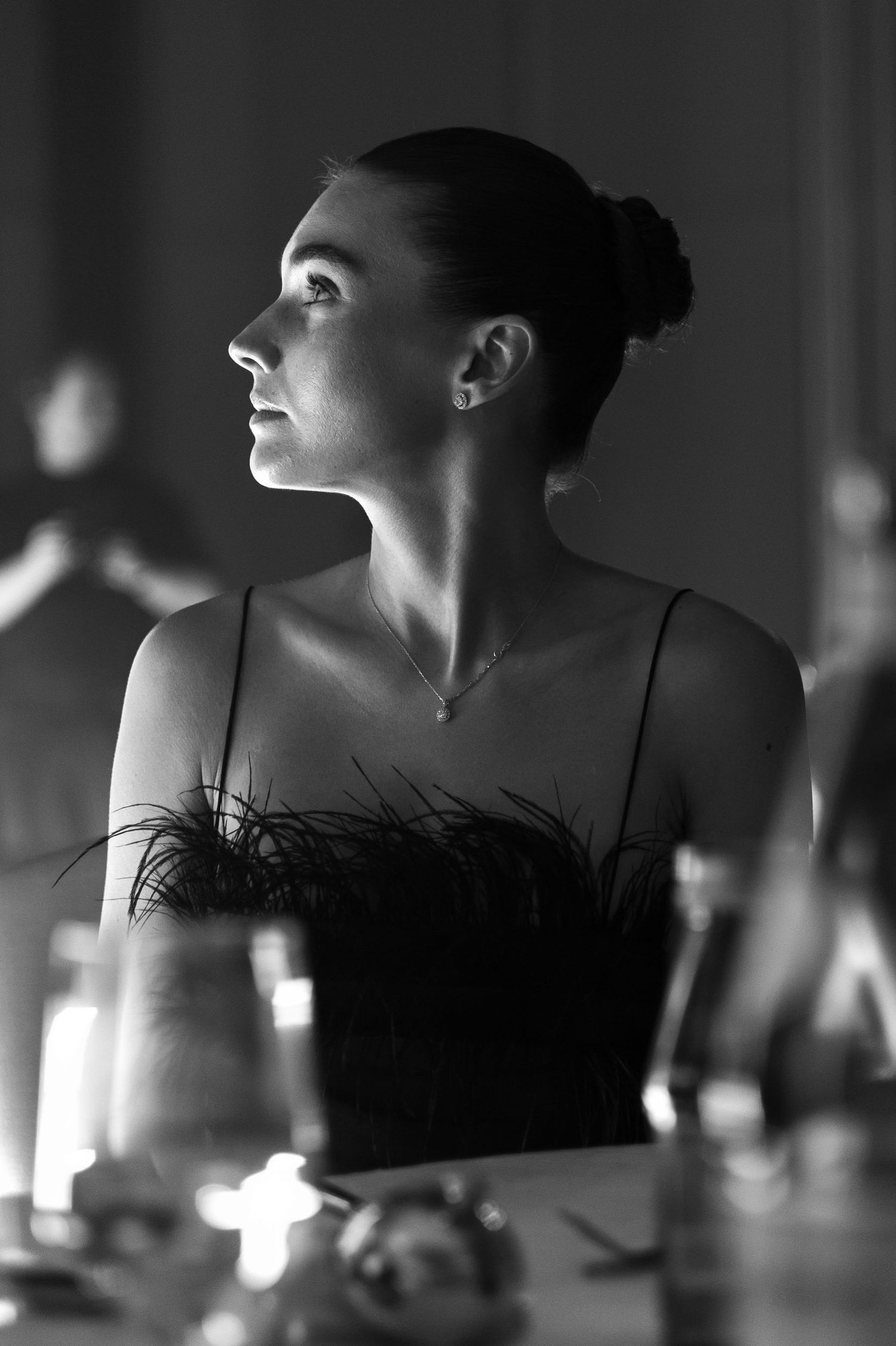 Dramatic black and white portrait of a dancer in a feathered dress looking upward in profile.