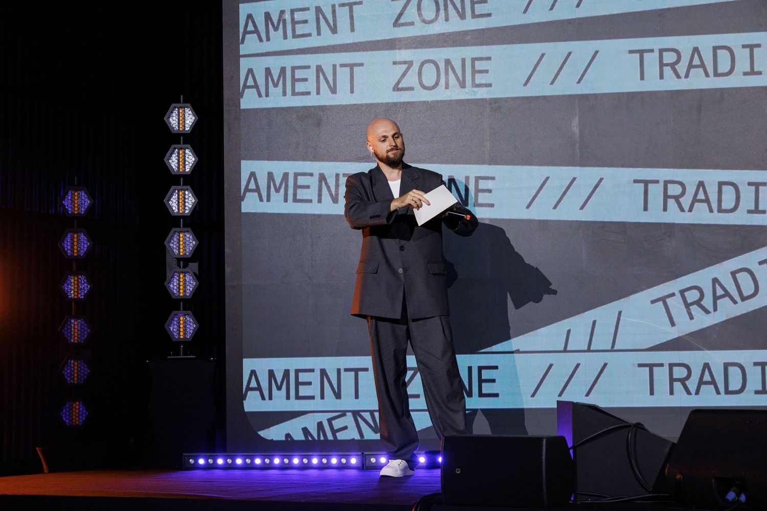 Speaker presents on stage with projected text displaying 'AMENT ZONE' in background.