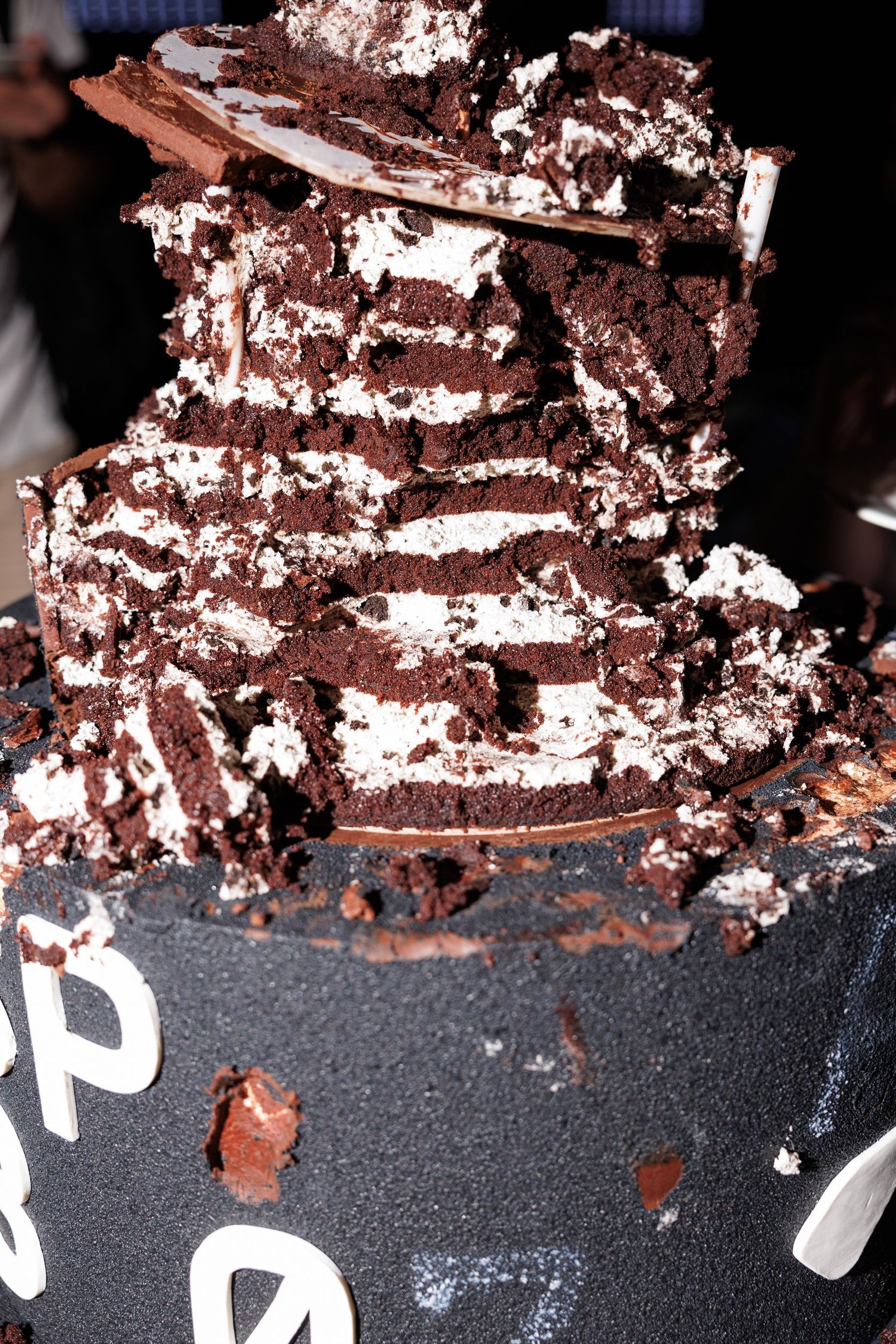 Close-up of layered chocolate cake with white cream filling on a dark surface.