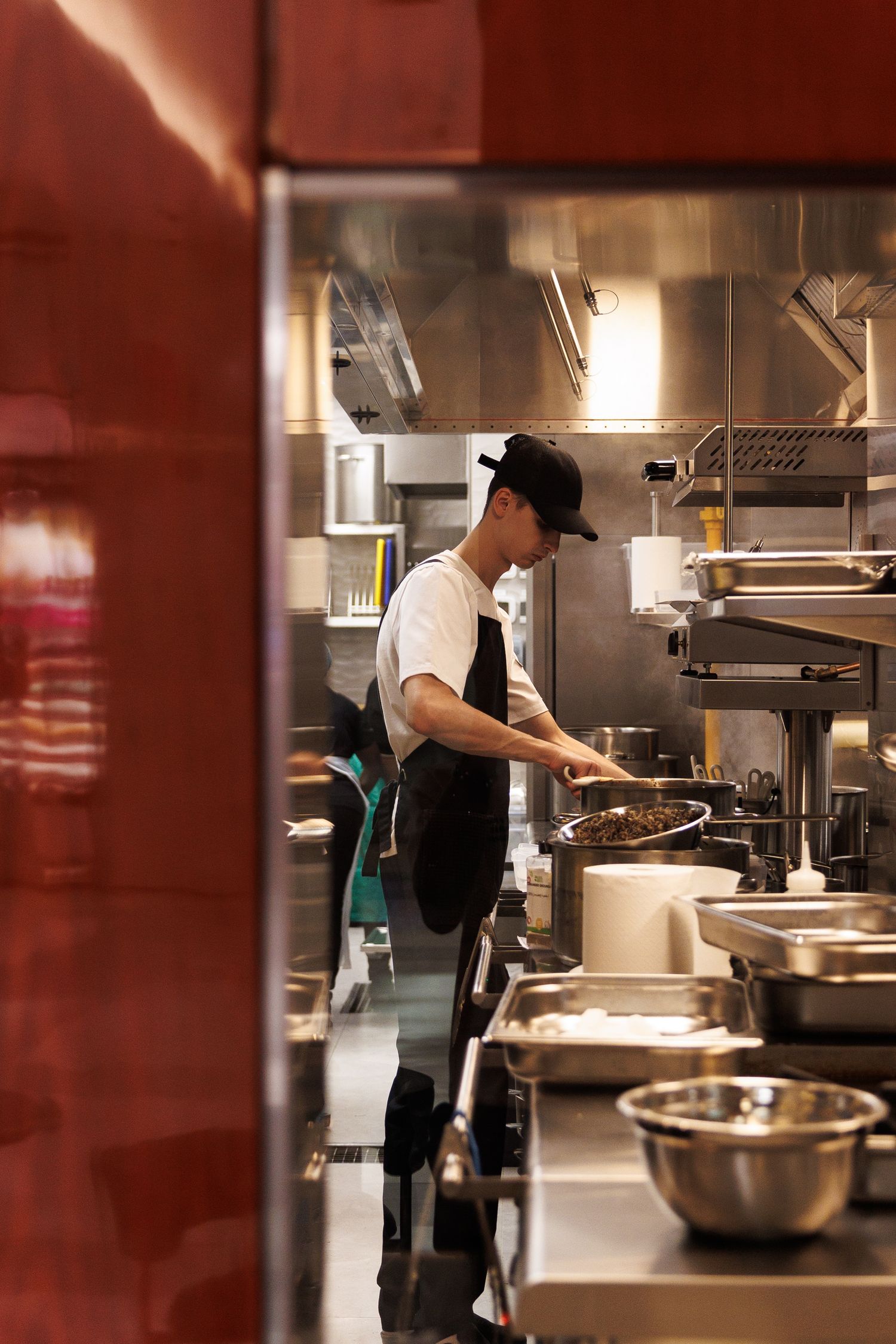 Commercial kitchen interior with staff working at stainless steel prep stations.