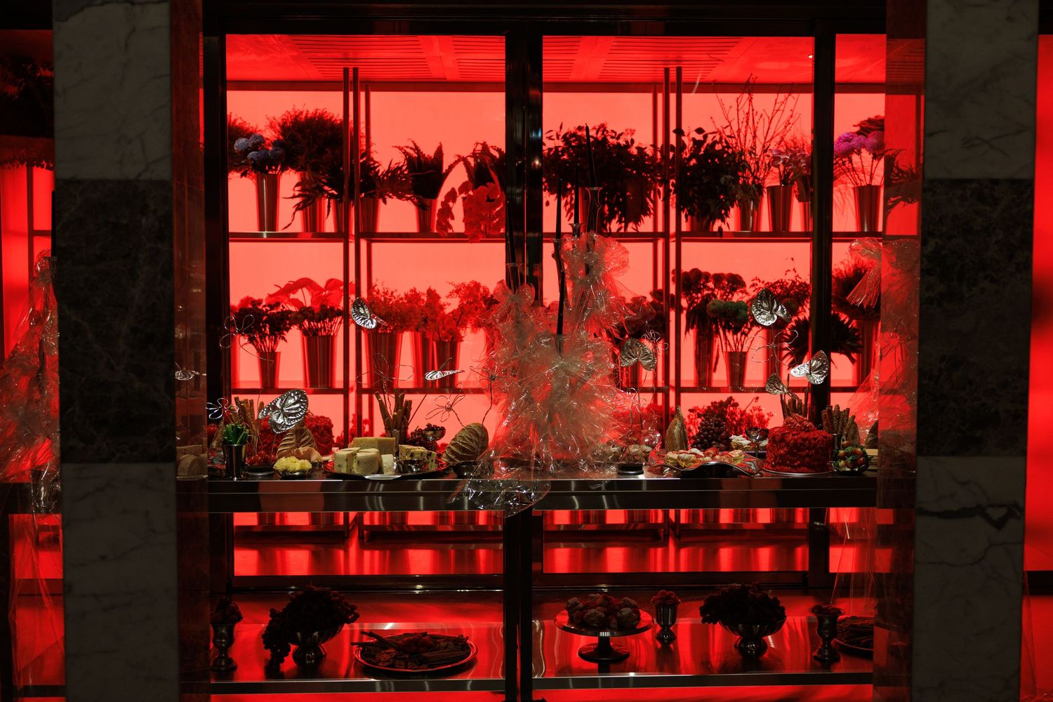 Modern restaurant interior illuminated with dramatic red lighting and palm tree silhouettes visible through windows.