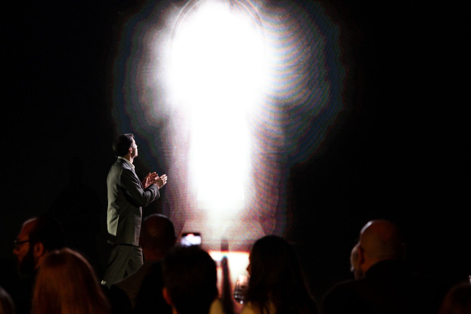 Silhouetted figures stand against bright stage lighting during a dramatic performance.