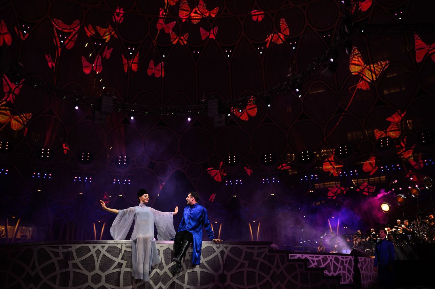 Theatrical performance with red butterfly decorations suspended above the stage in dramatic lighting.