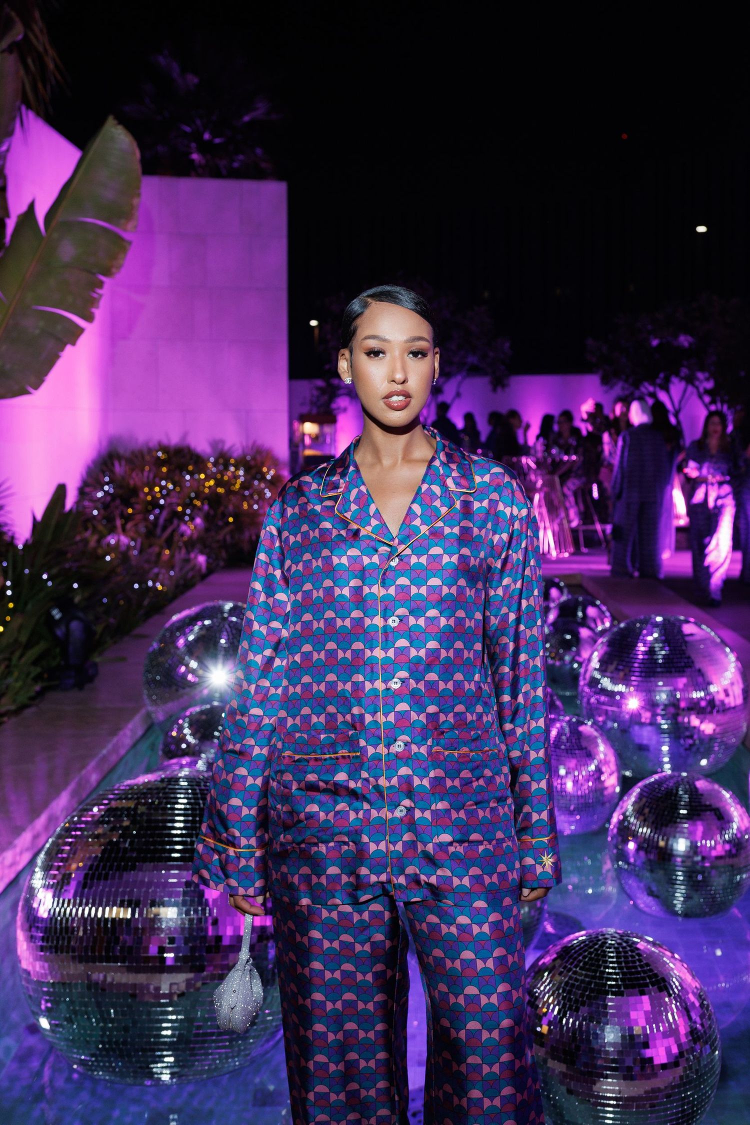 Fashion models in coordinated blue outfits pose with disco balls under purple lighting.