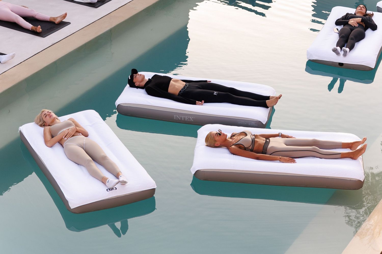 Multiple people relaxing on white loungers beside a turquoise pool.