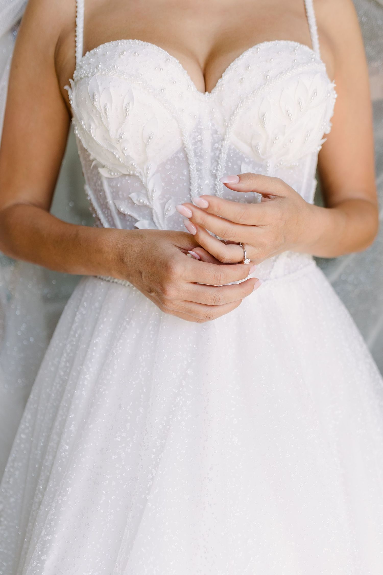 Close-up detail of bride's hands on white beaded corset wedding dress bodice.