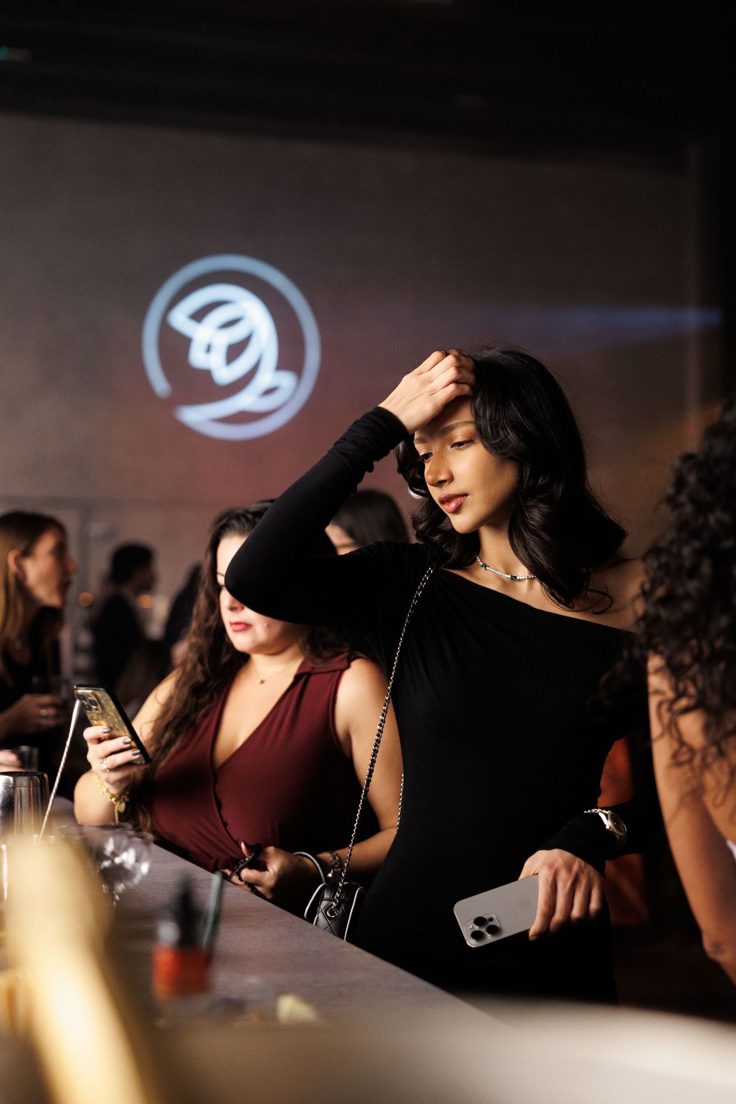 Atmospheric nightclub scene with projected logo and people enjoying drinks at bar.