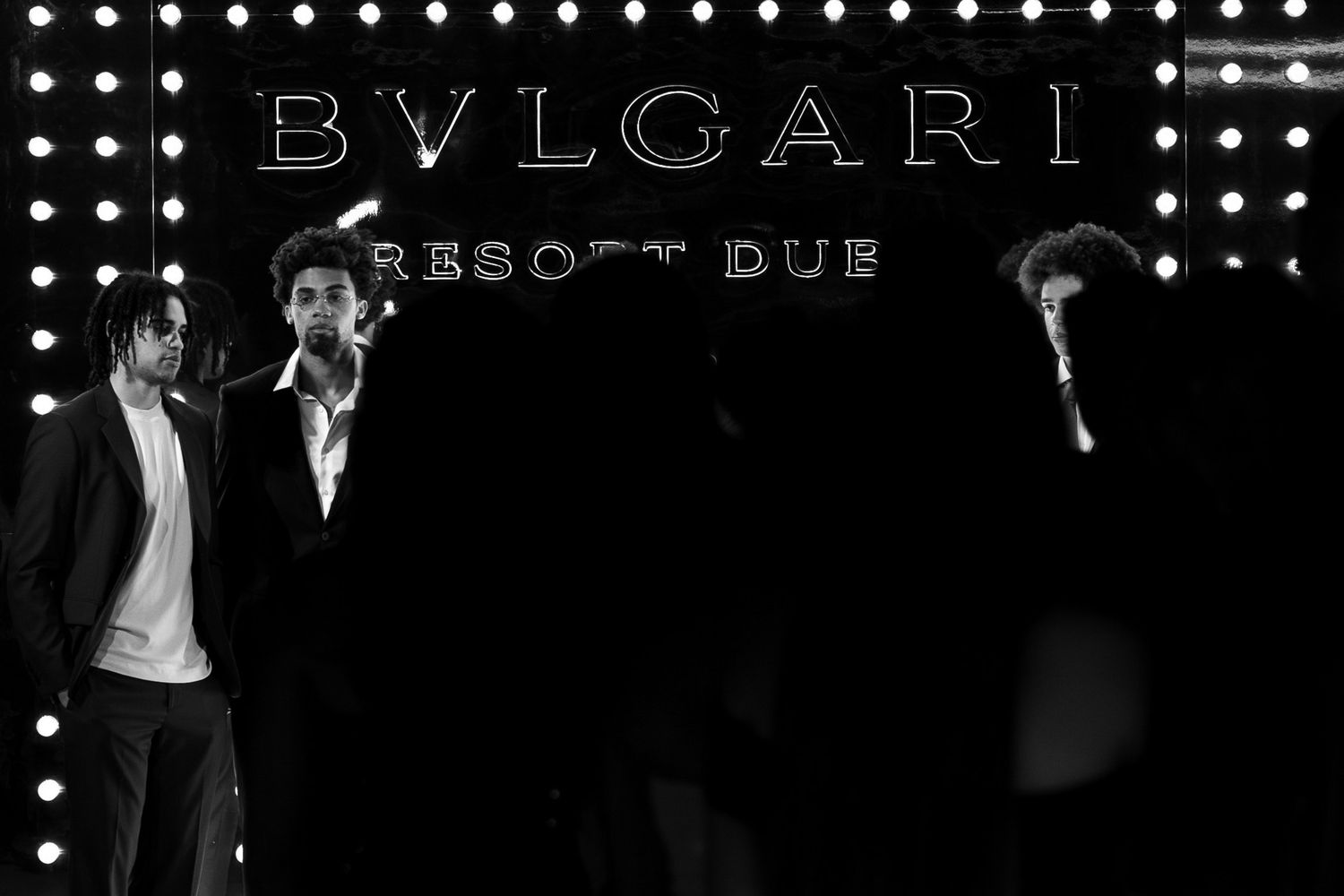 Black and white photo of Bvlgari event with illuminated logo and silhouetted figures.