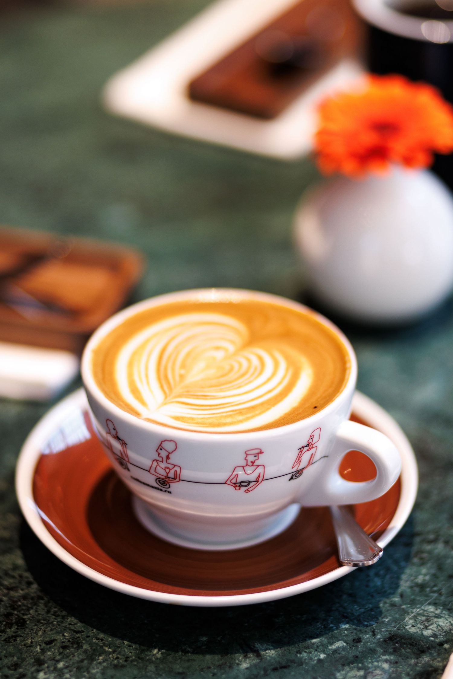 A coffee cup with heart-shaped latte art and decorative pattern on a green marble surface.