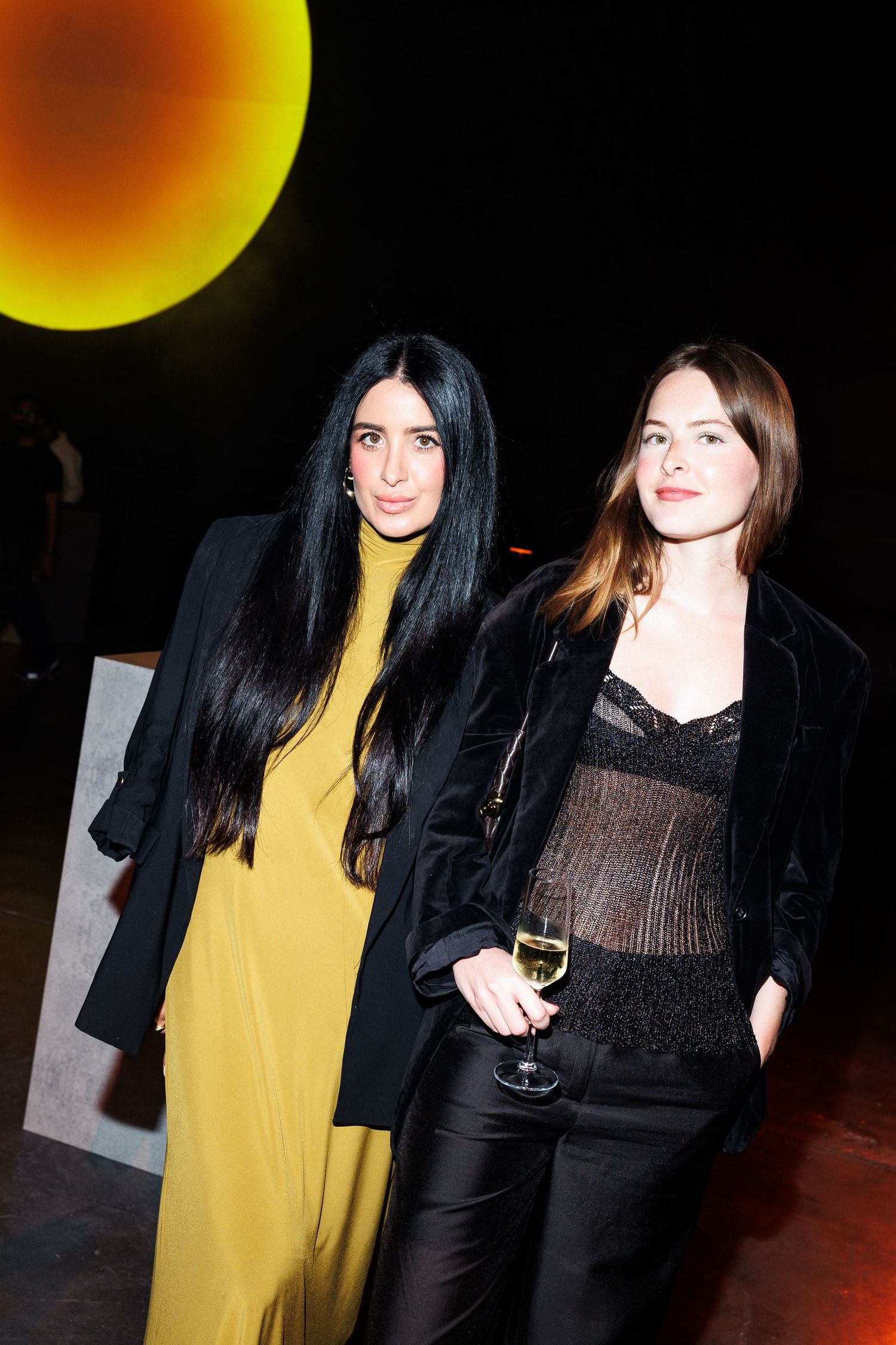 Two women in contrasting outfits pose at an evening event.