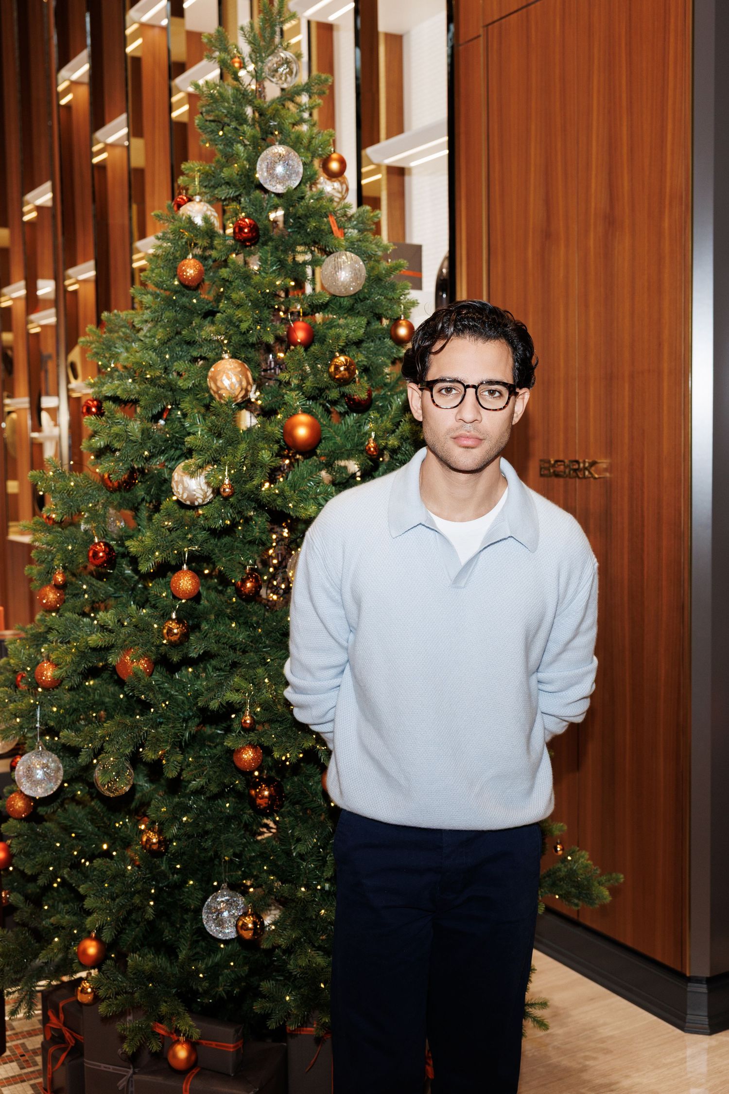 Person in light sweater posing near decorated Christmas tree in retail environment.