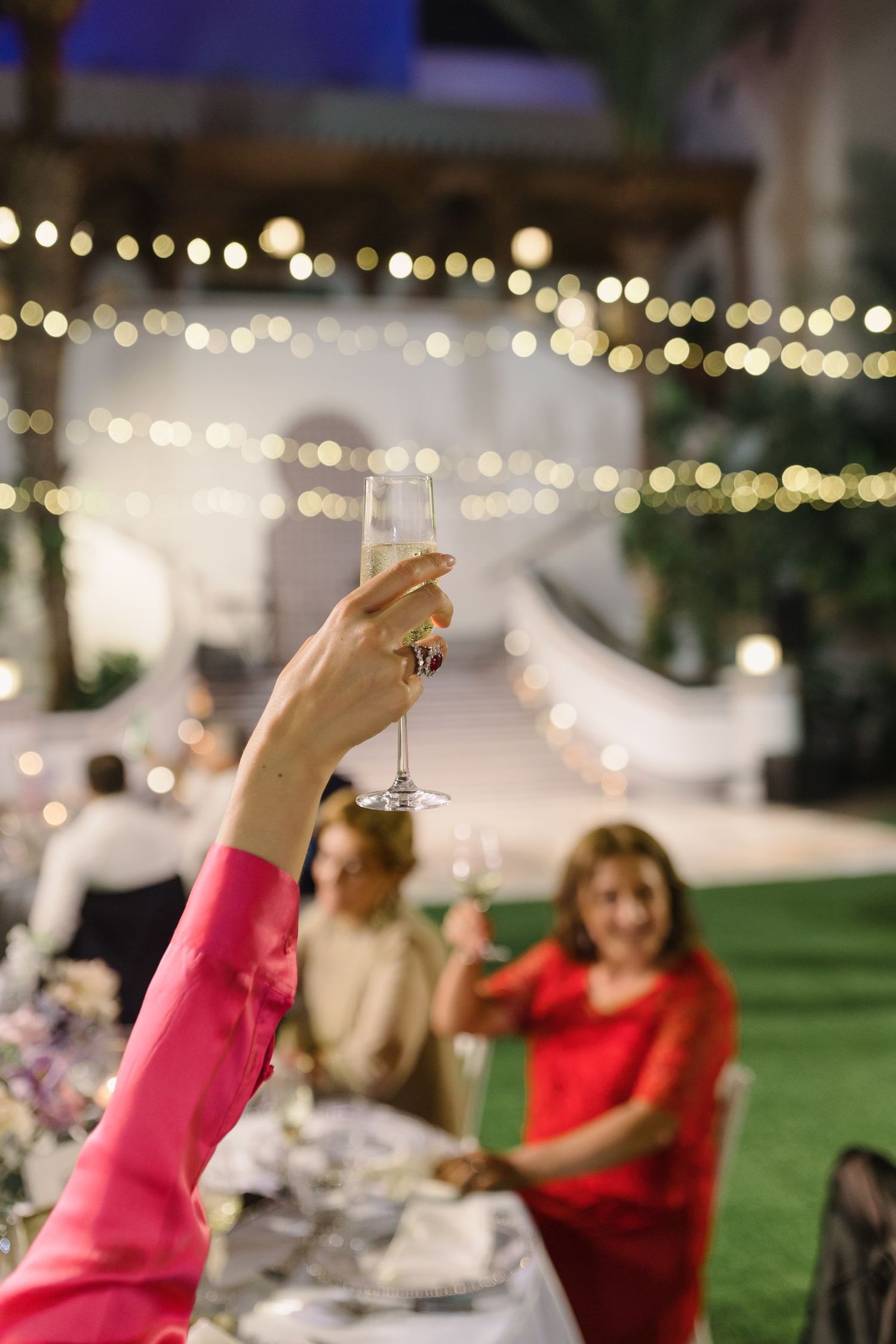 Wedding guests raise their glasses in a celebratory toast during an outdoor reception.