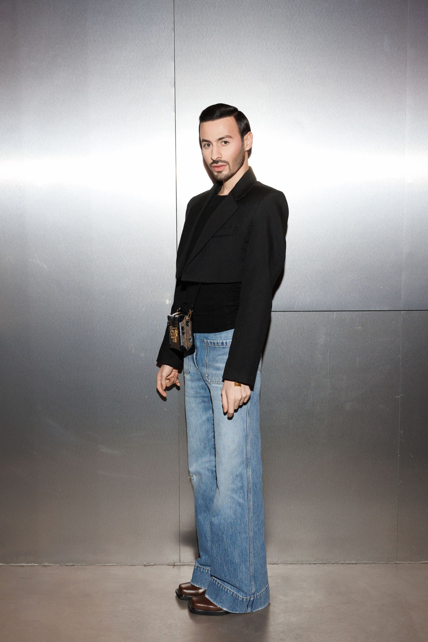 Person wearing black top and denim skirt poses against grey studio backdrop.