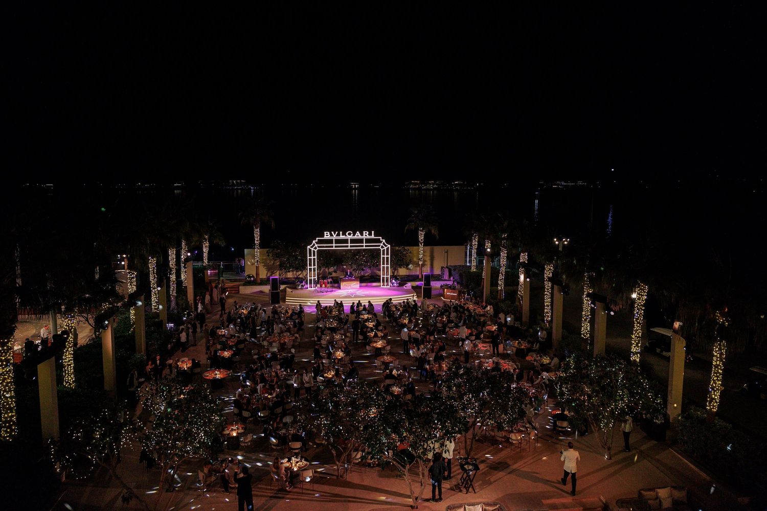 Wide view of an elegant outdoor event venue with stage and seating arrangements at night.
