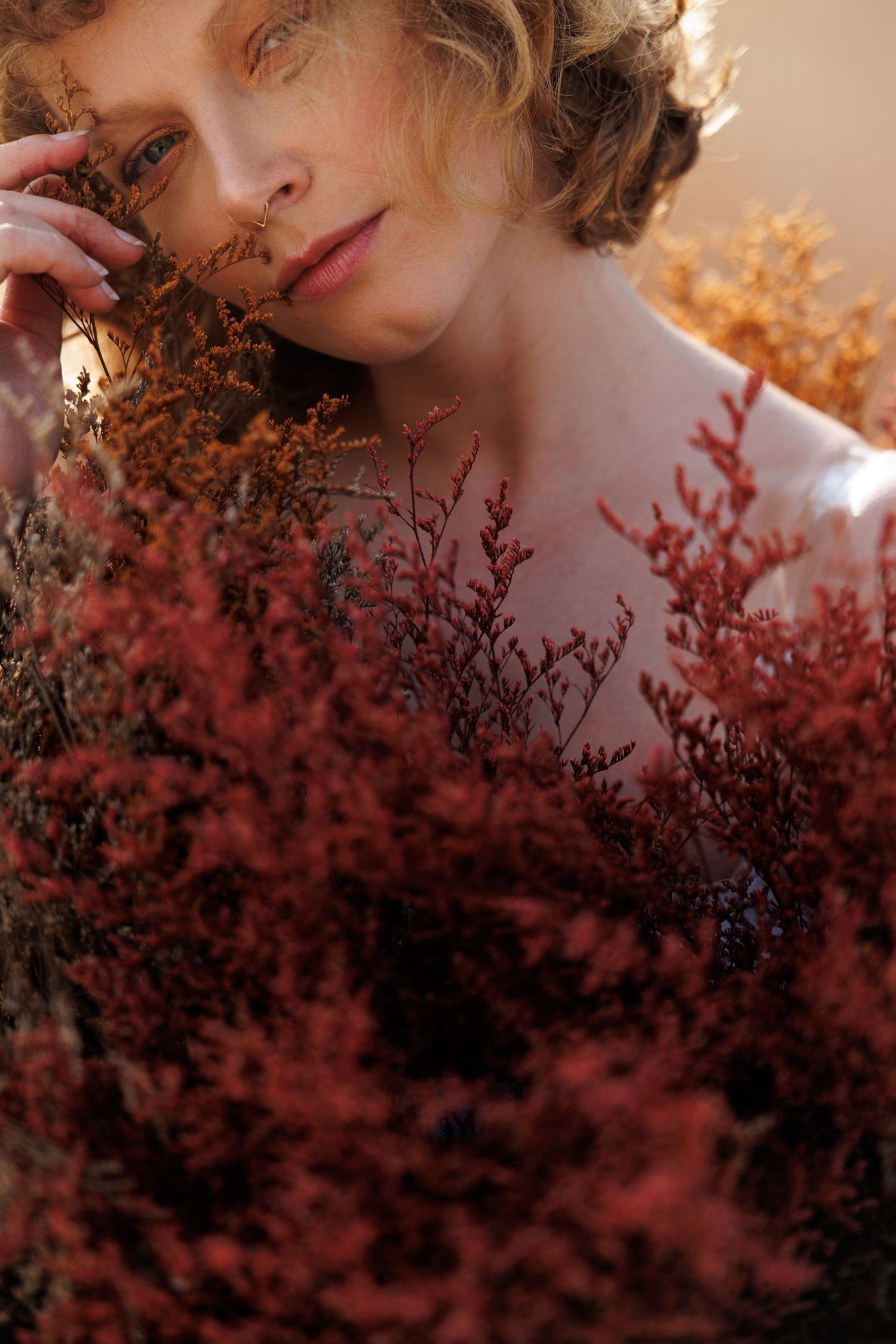 Artistic portrait with red dried flowers in soft natural lighting creating a dreamy atmosphere.