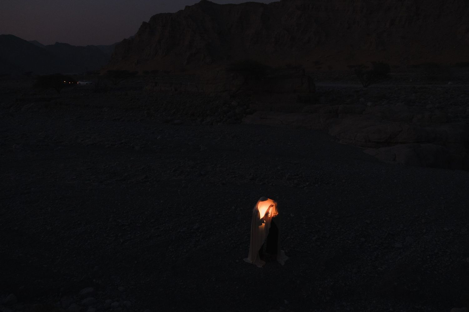 Dark landscape photograph with glowing orange lights visible in distance.