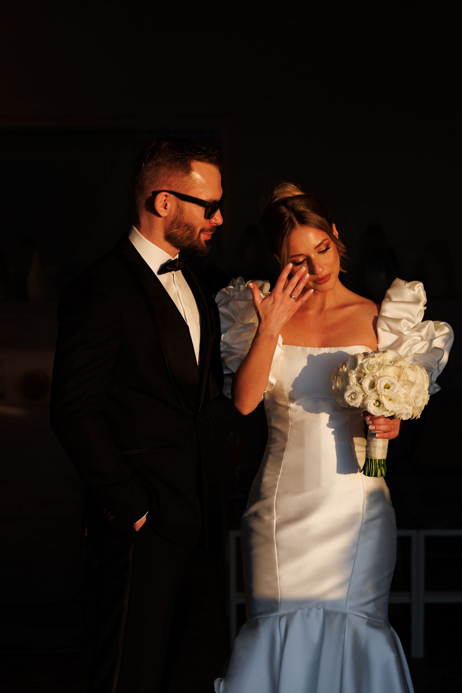 A romantic wedding couple embraces in formal attire during an evening photoshoot.
