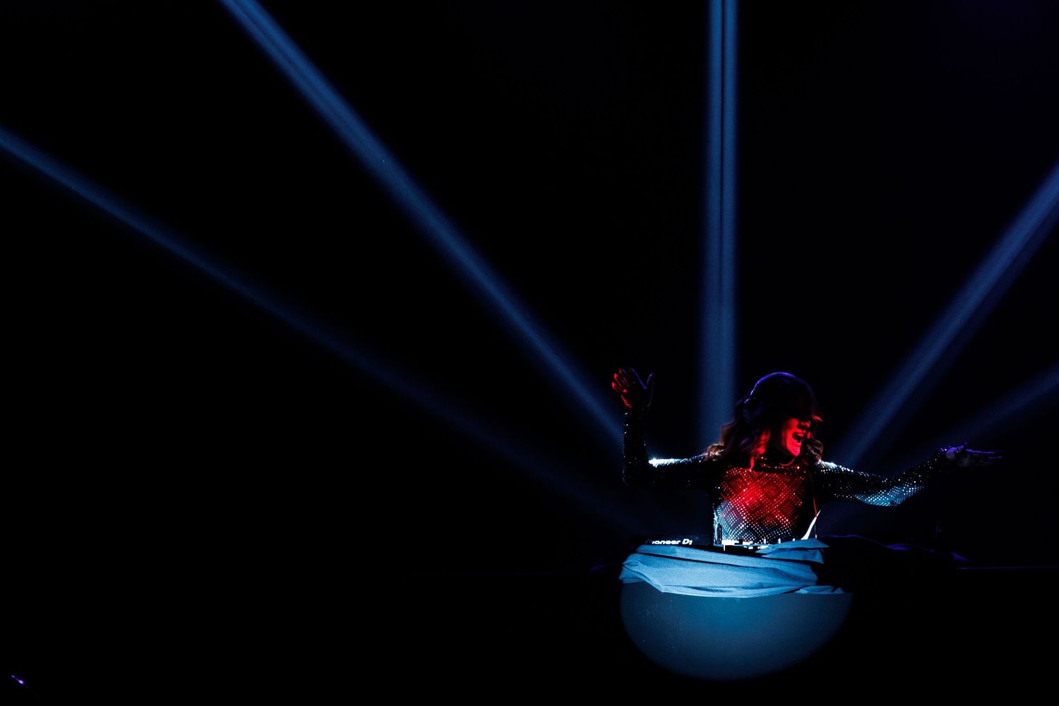 Blue laser light beams create geometric patterns against a dark background during a performance.