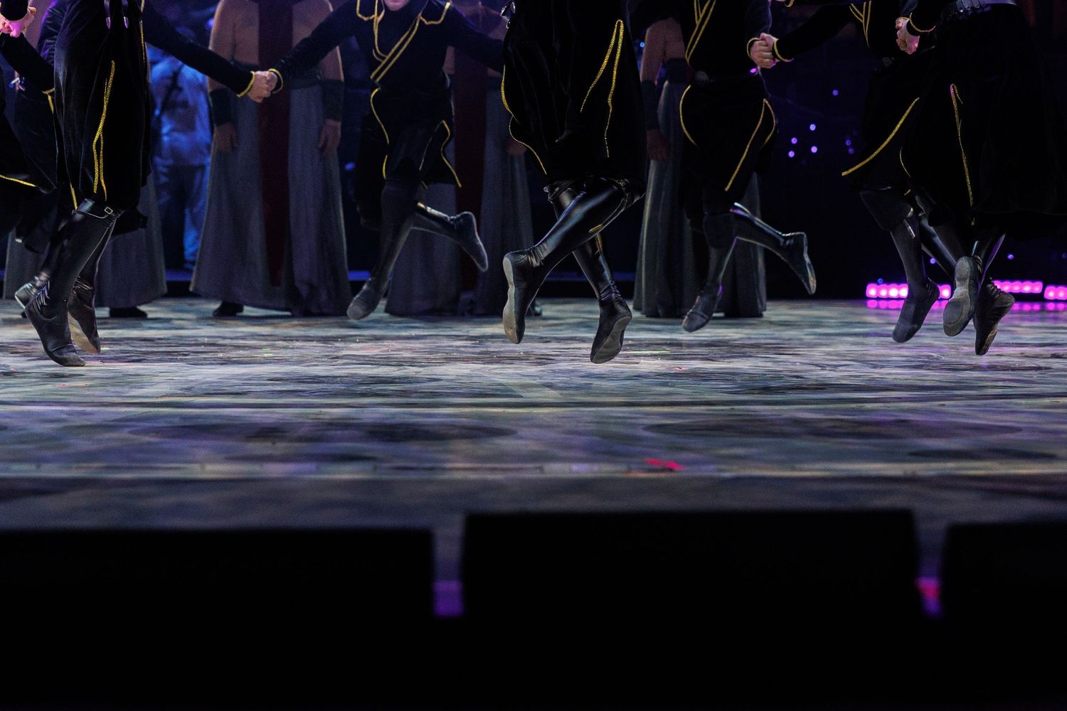 Performers in dark costumes moving across a stage with purple accent lighting.