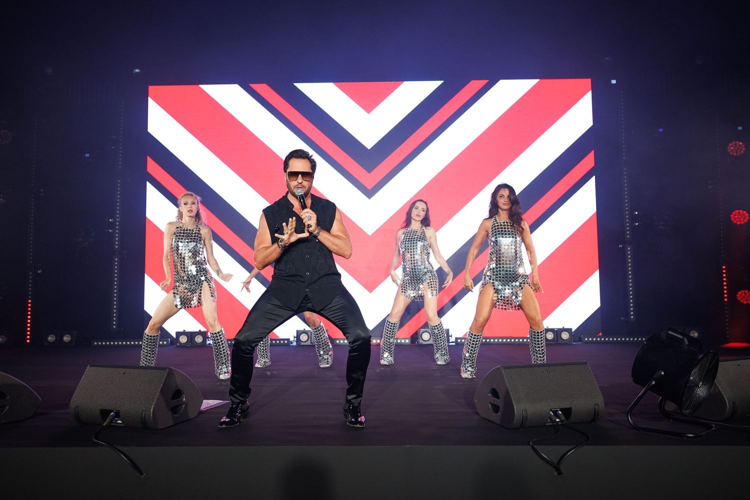 Dynamic stage performance with dancers against geometric red white and blue backdrop.