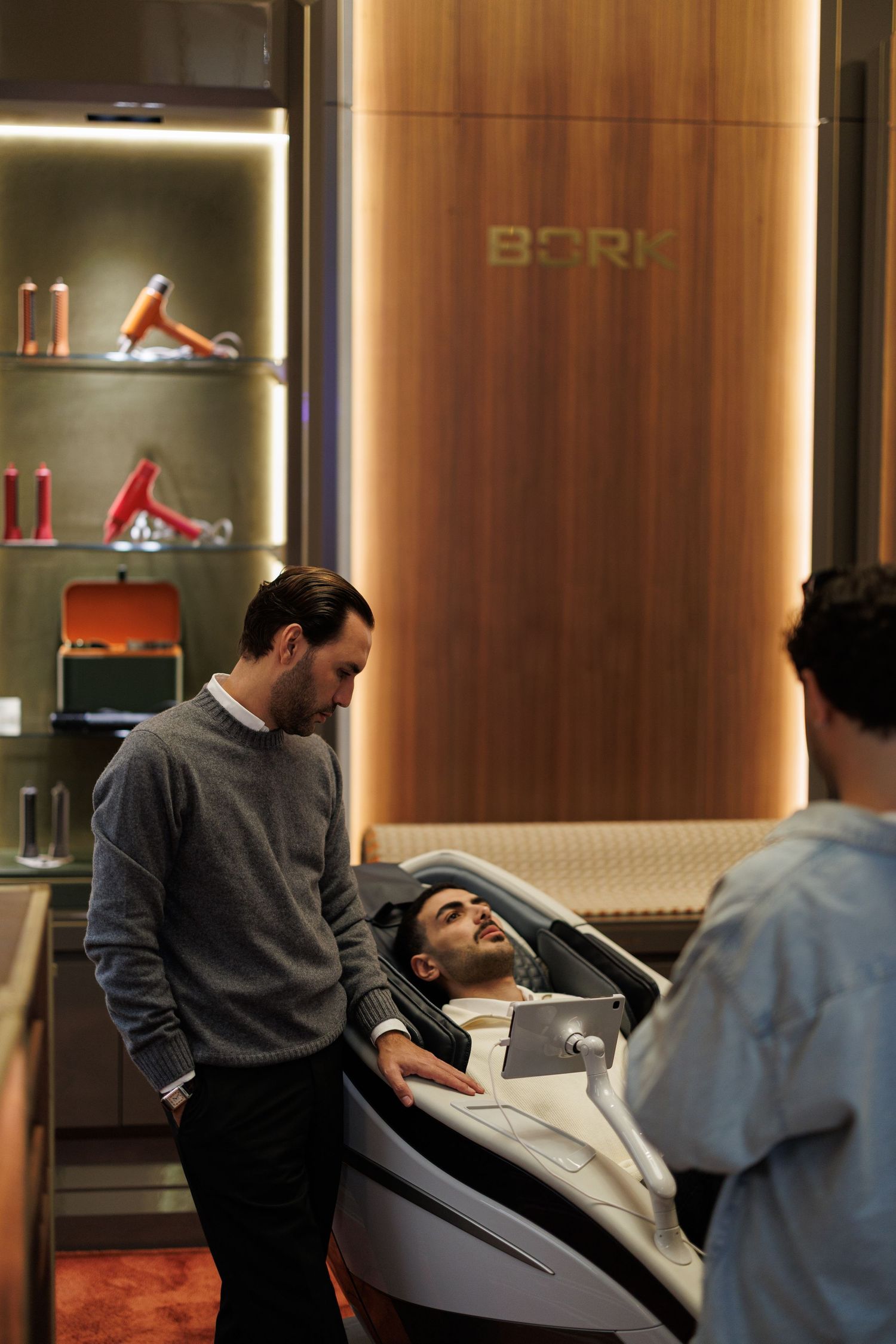 People relaxing in modern salon chairs with warm lighting and wood-paneled walls.