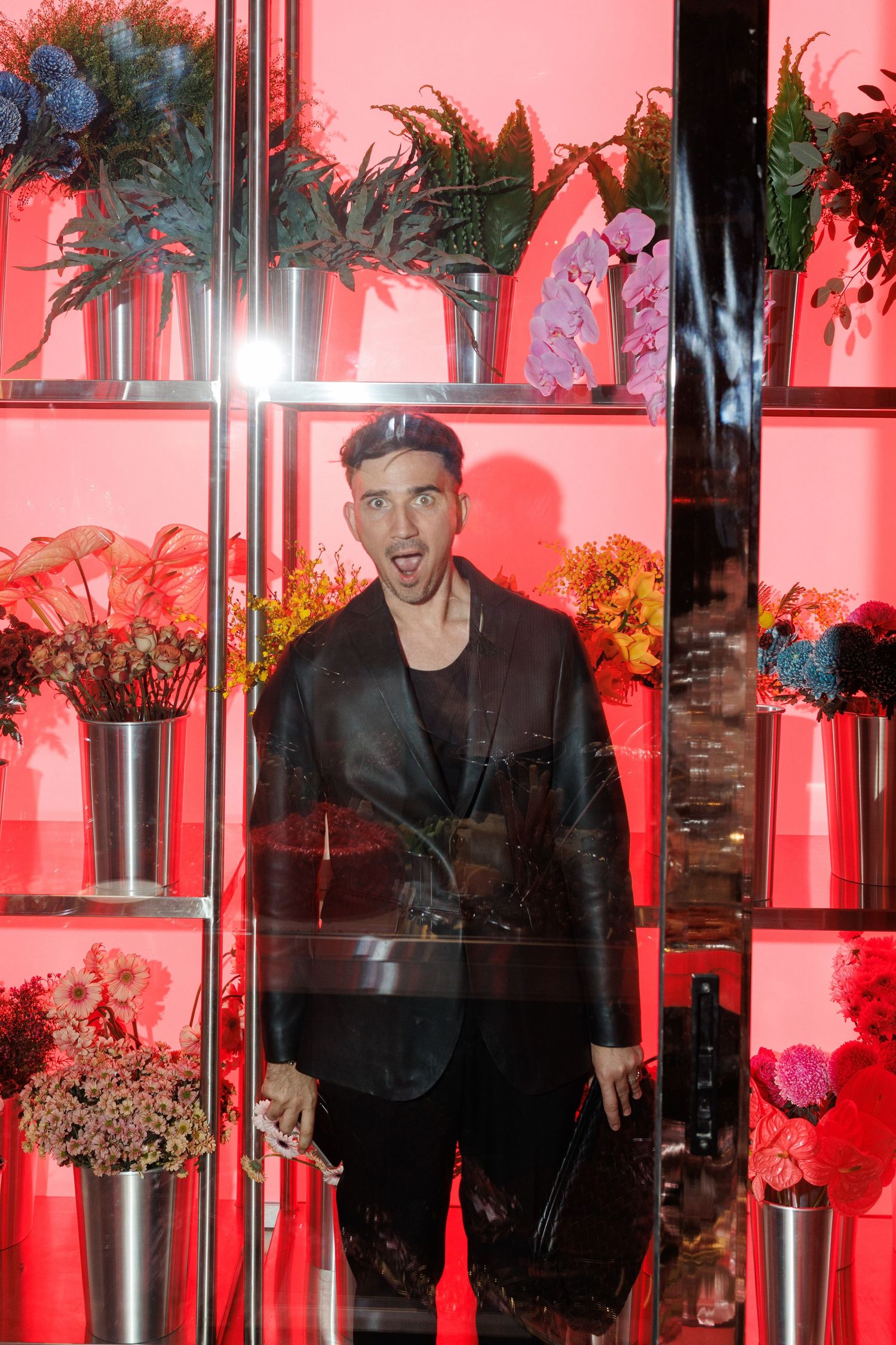 Display of floral arrangements on illuminated shelves bathed in red lighting.