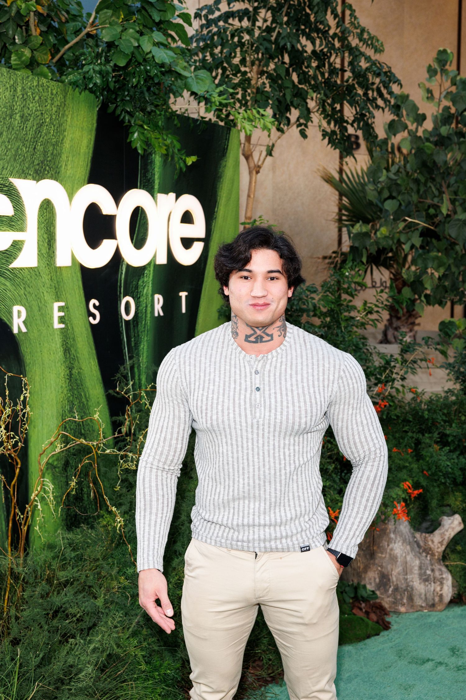 A person in a white striped sweater stands in front of a green Encore Resort sign surrounded by lush greenery.