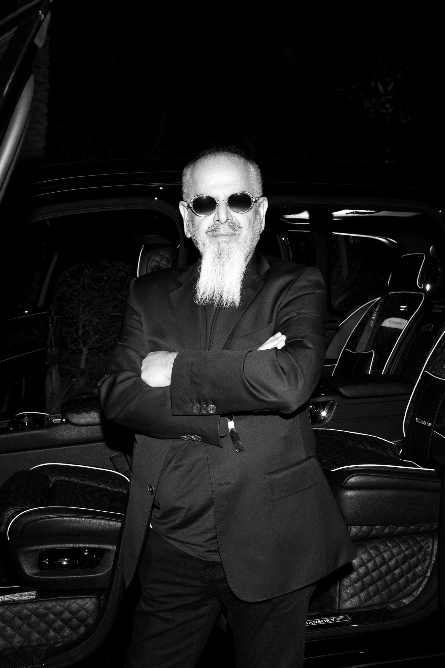 Person in dark clothing sitting against a luxury car at night.