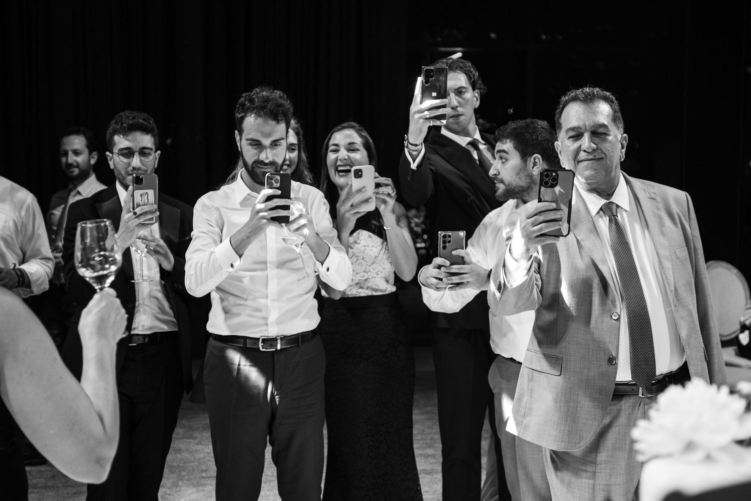 Wedding guests in formal attire hold up their phones to capture a moment at the reception.