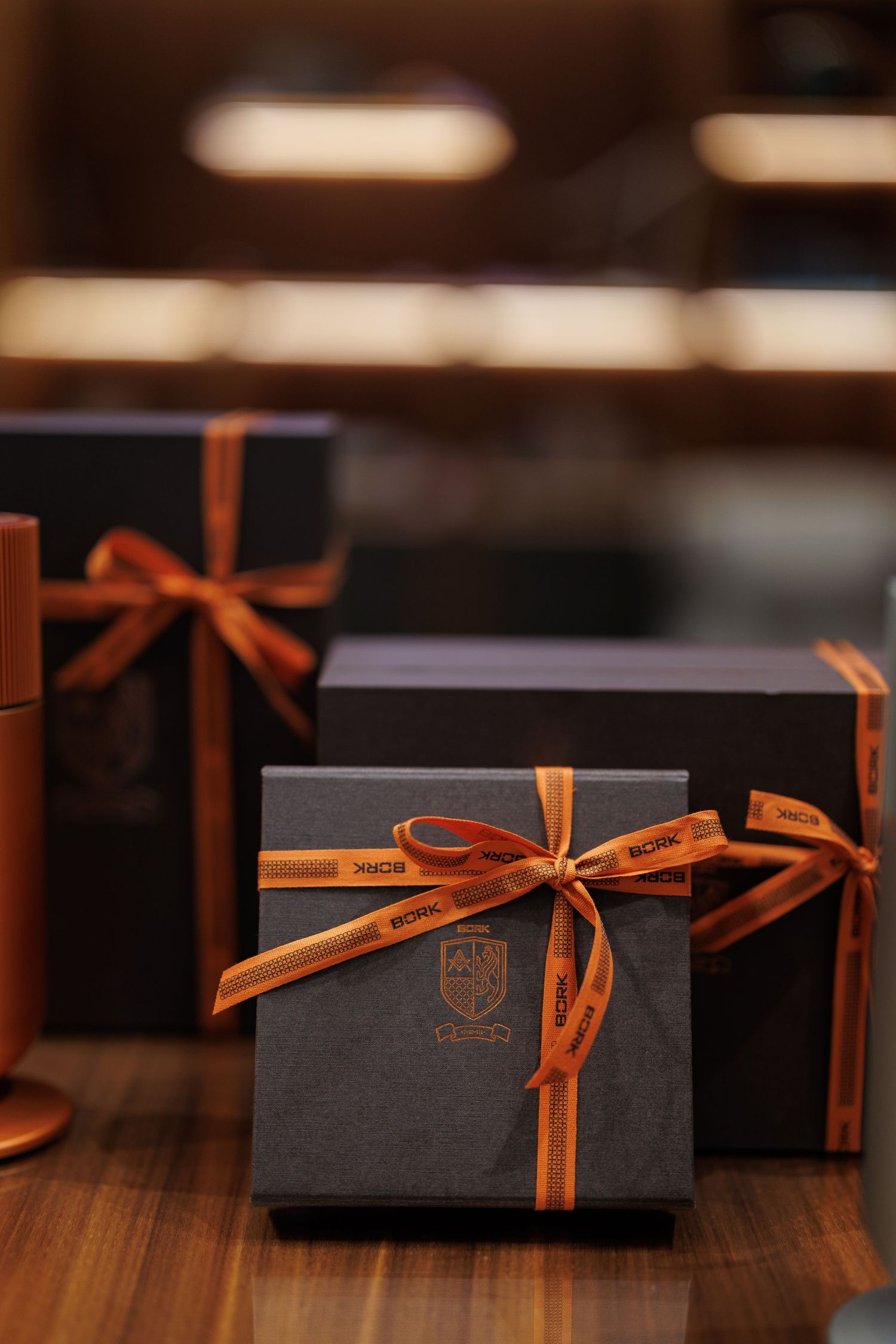 Elegant black gift boxes with orange ribbon bows arranged in a row on a wooden surface.