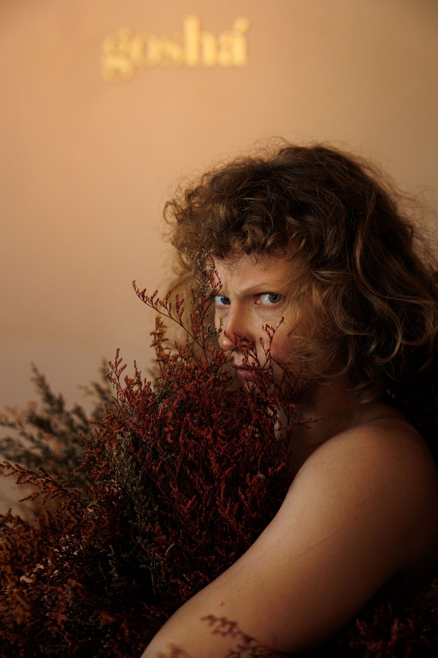 Moody portrait with burgundy dried flowers and 'gosha' text illuminated in background.