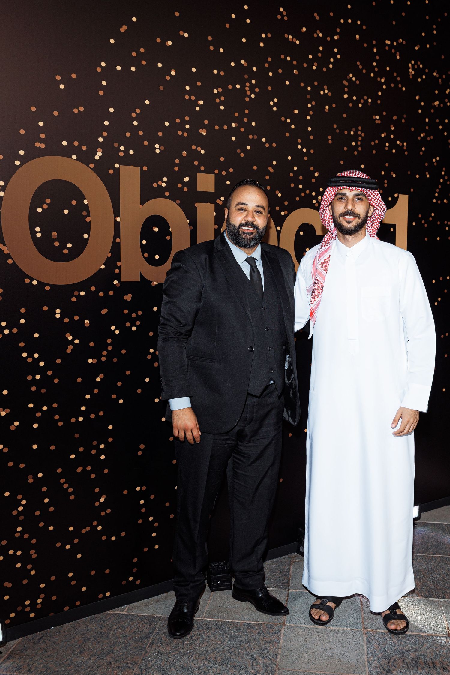 Event attendees in traditional Middle Eastern and Western formal attire against a sparkly backdrop.