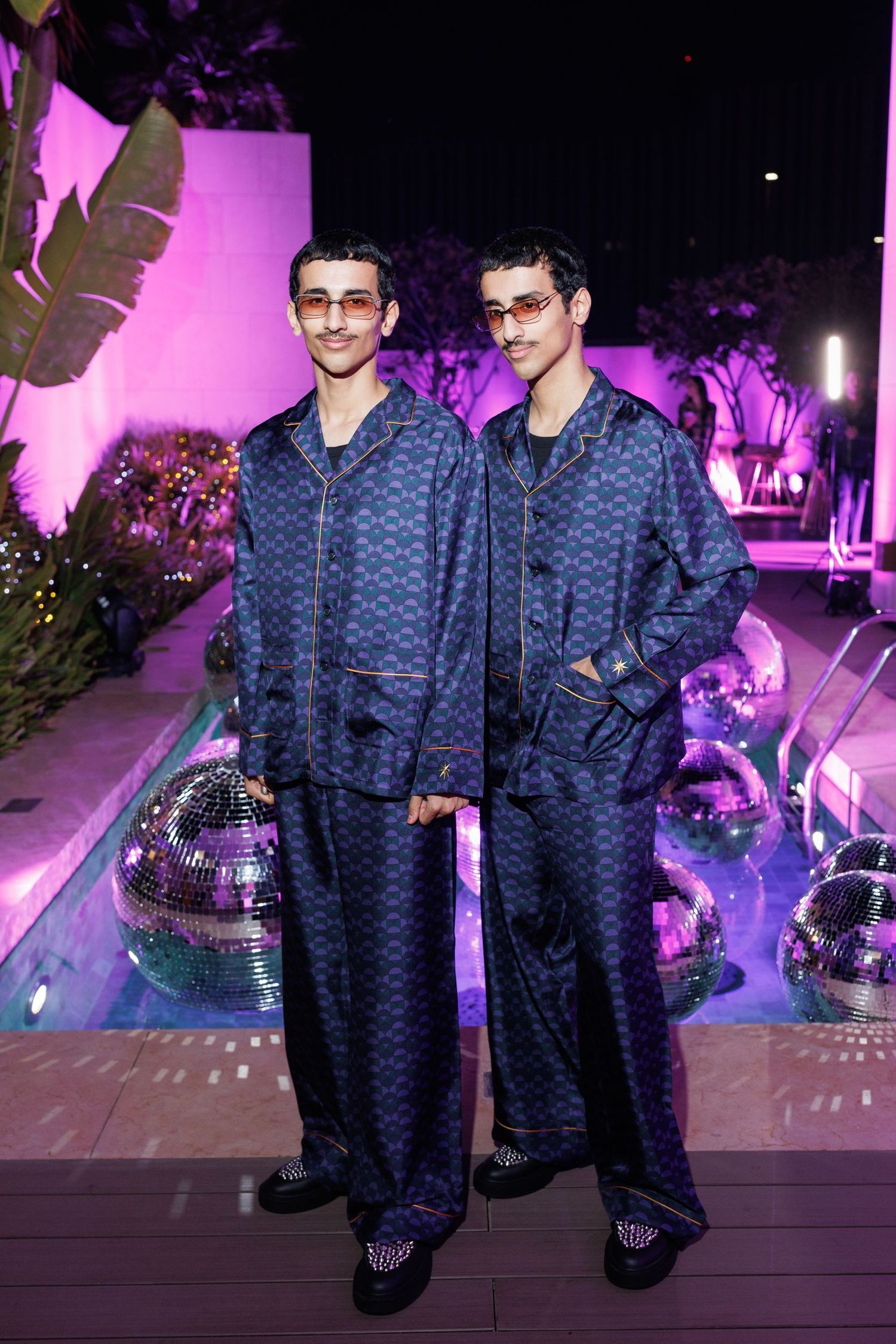Party scene with people in matching blue patterned outfits under purple lighting.
