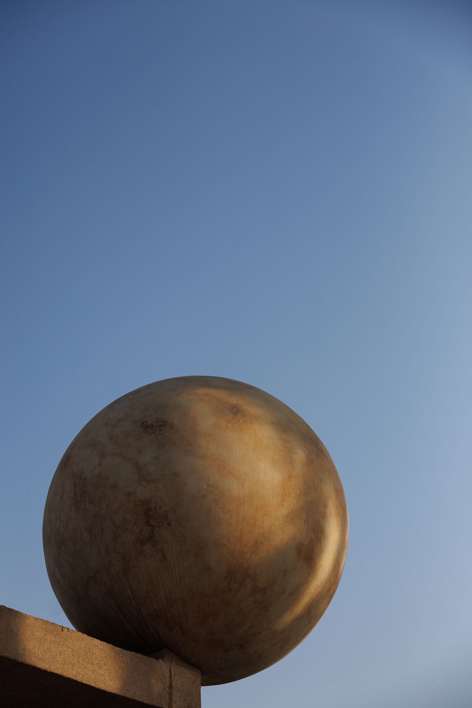 Abstract architectural detail of curved bronze structure against blue sky.
