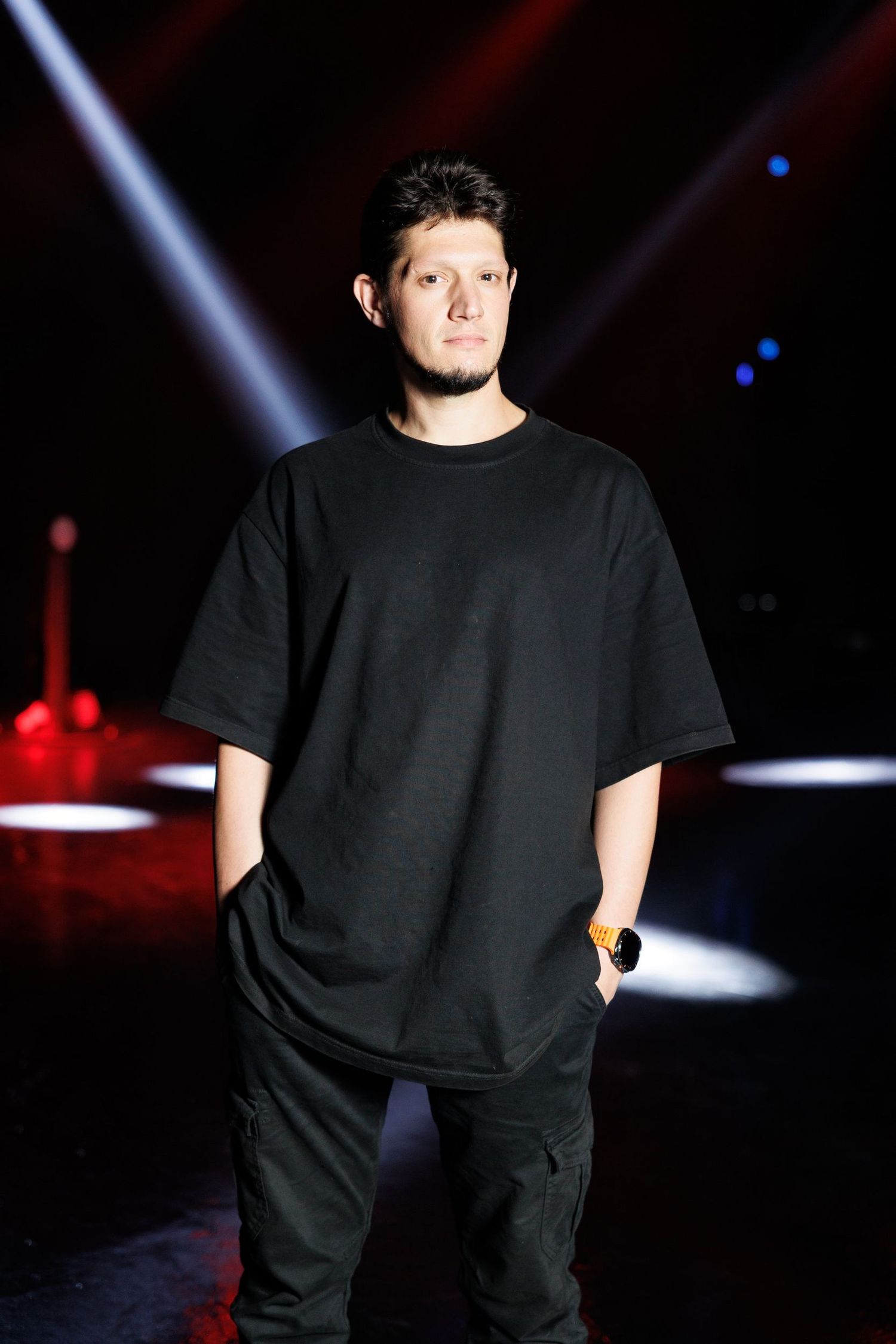 Performer in casual black outfit standing under theatrical lighting.