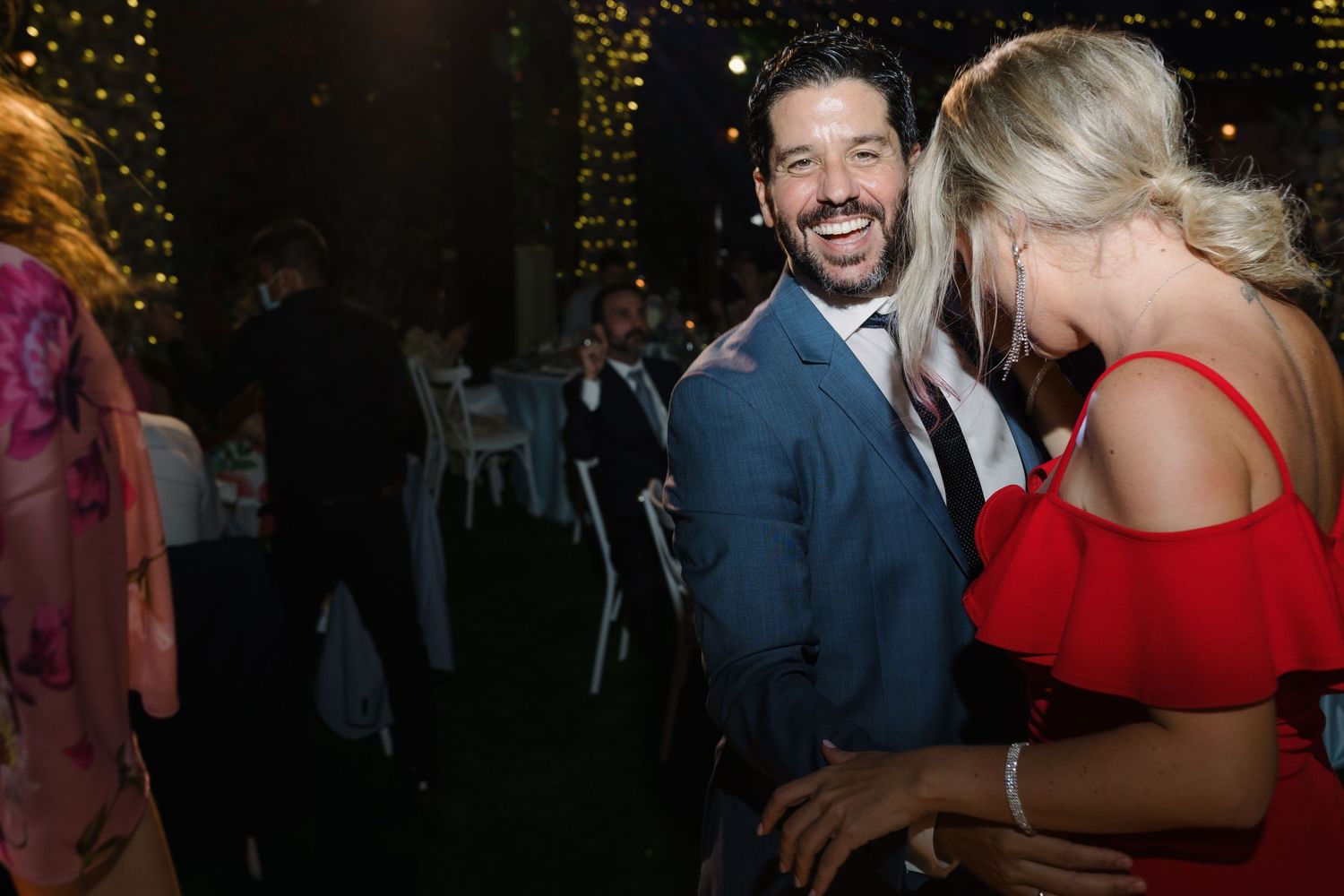 Wedding reception guests dancing and celebrating under string lights at night.