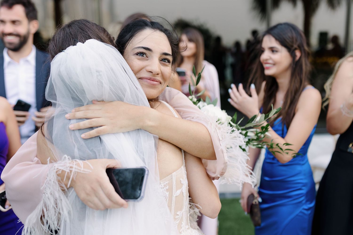 Wedding guests embrace and celebrate during an outdoor reception.