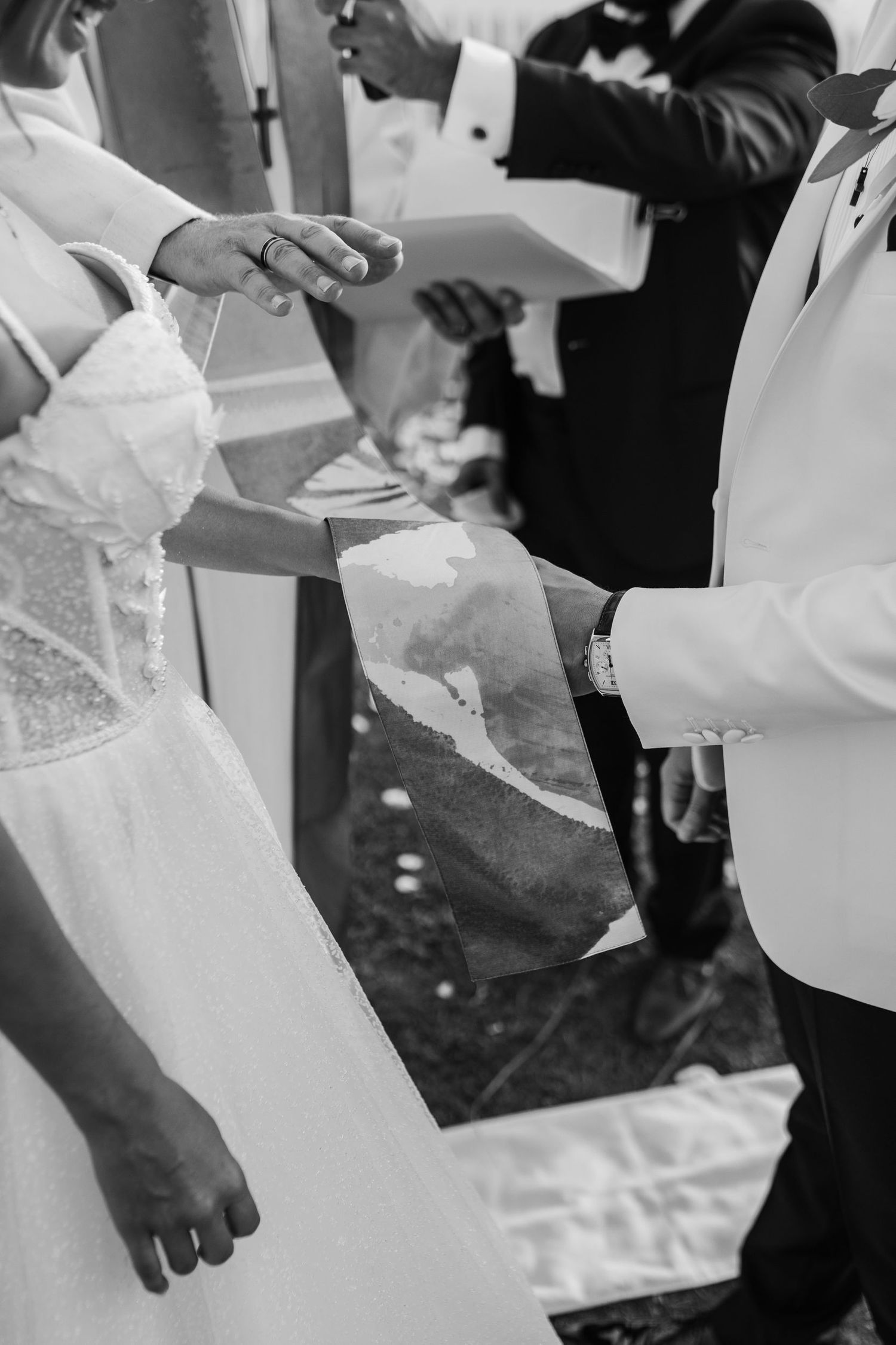 Black and white detail shot of formal wedding attire at an outdoor celebration.