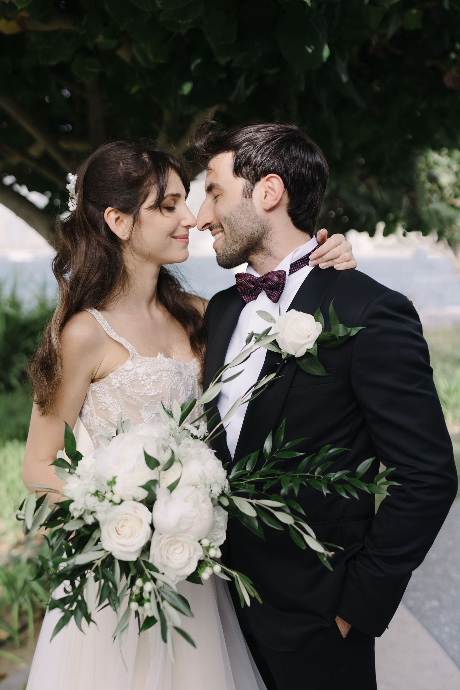 Intimate wedding portrait with white roses and greenery bouquet in natural setting.