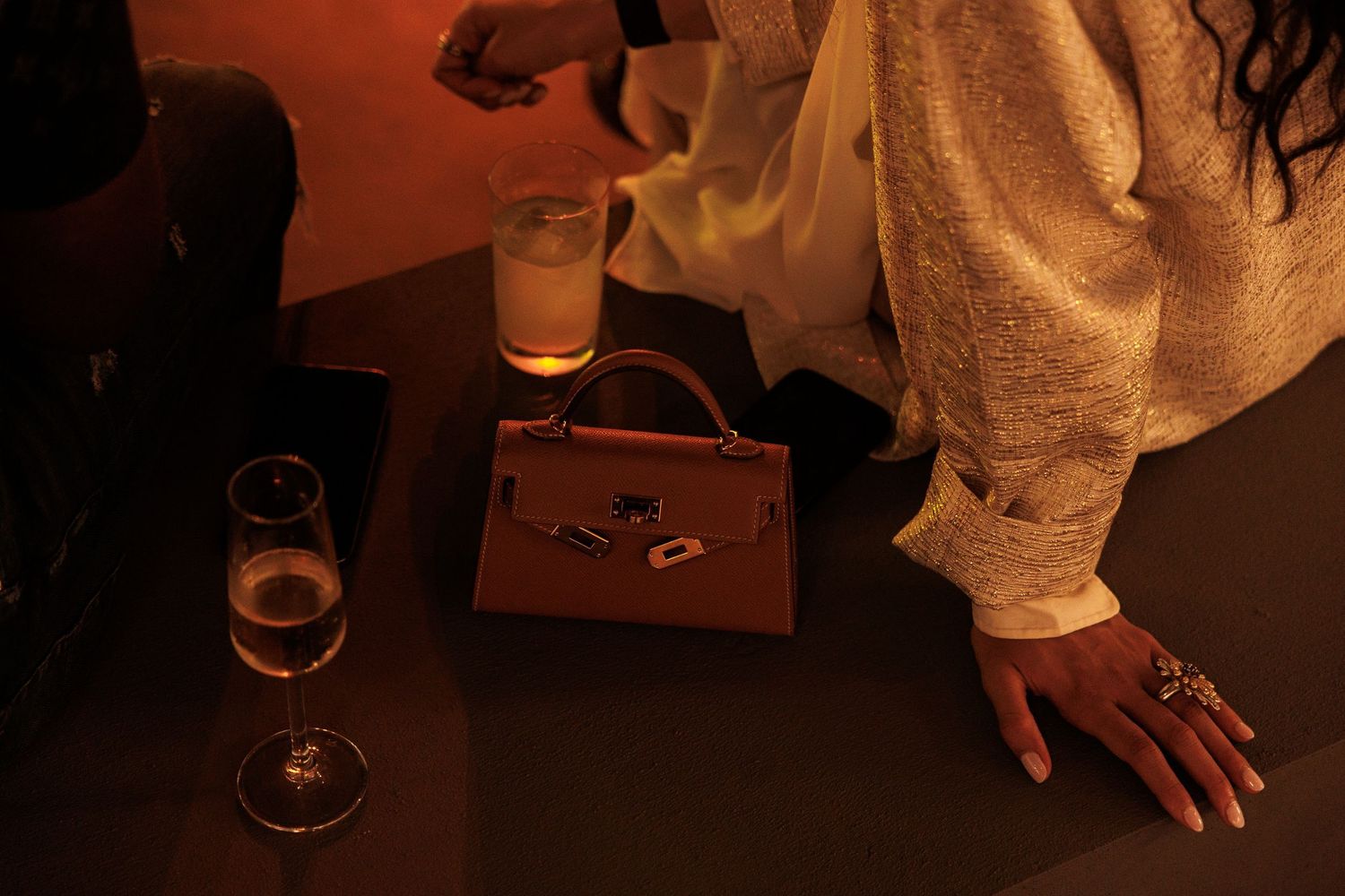 Hands reaching for drinks on a wooden table in moody lighting.