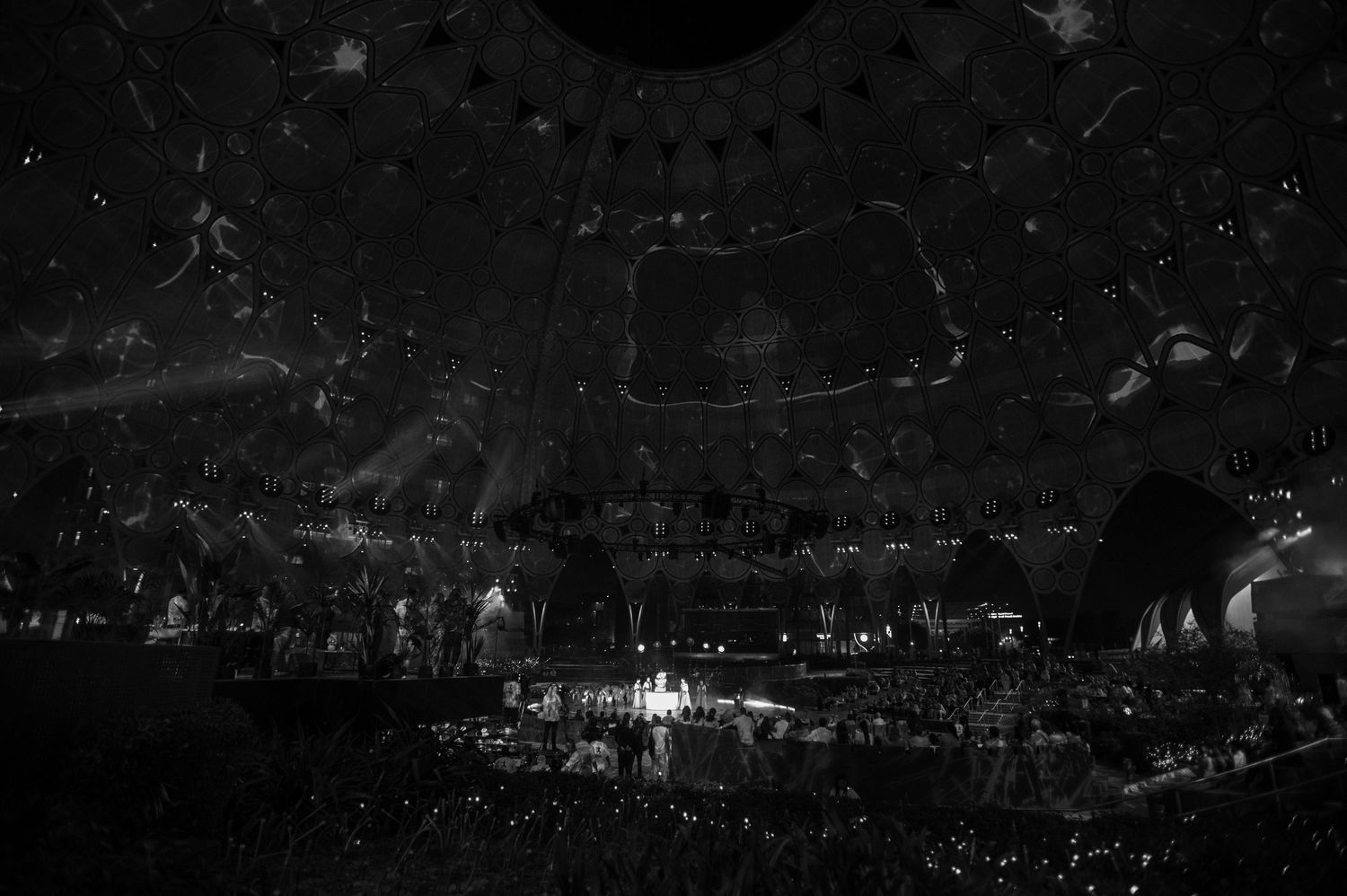 Wide shot of darkened arena with distant stage lights and crowd silhouettes.