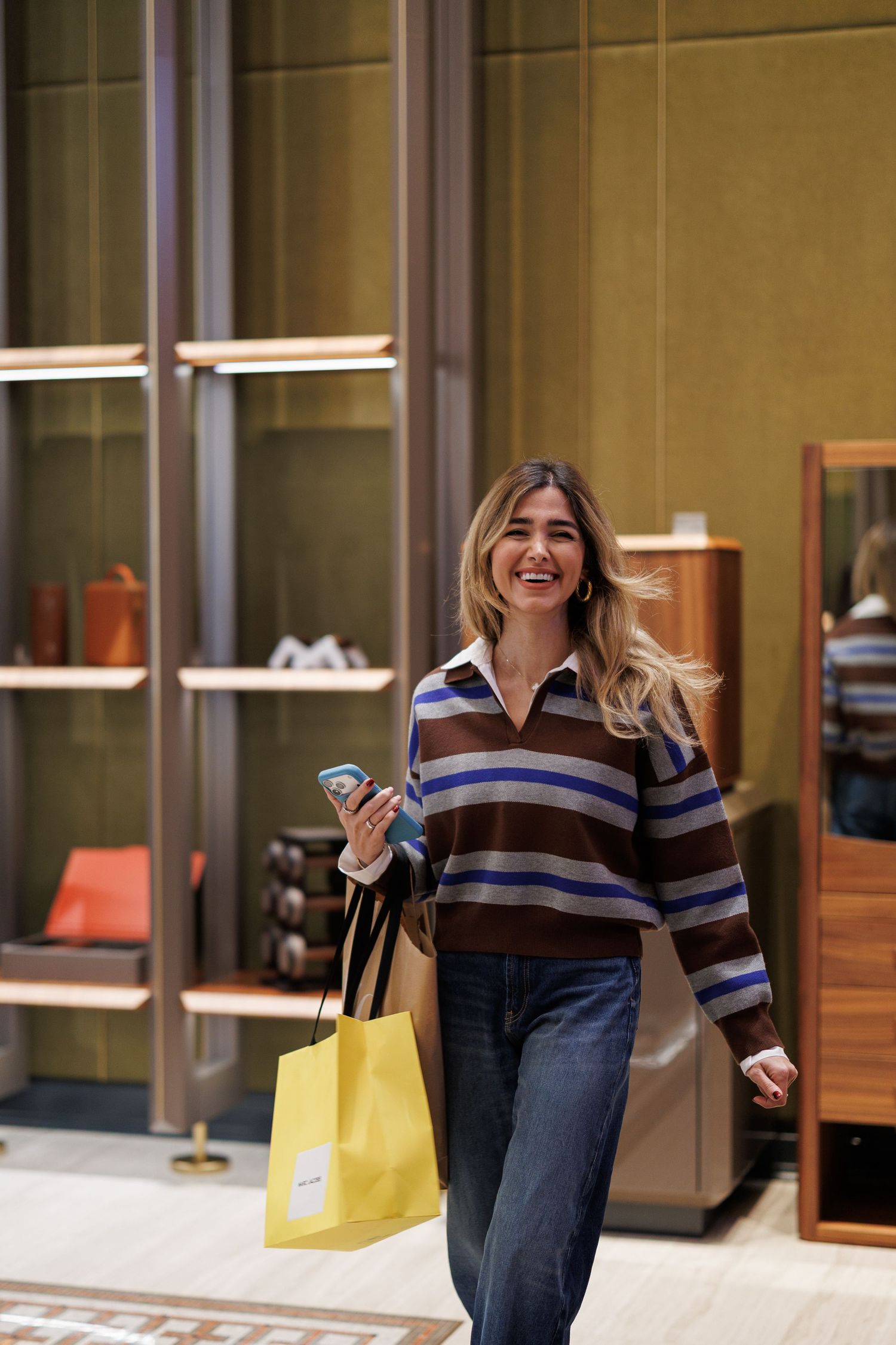 Person walking through a modern shopping area carrying yellow shopping bags.
