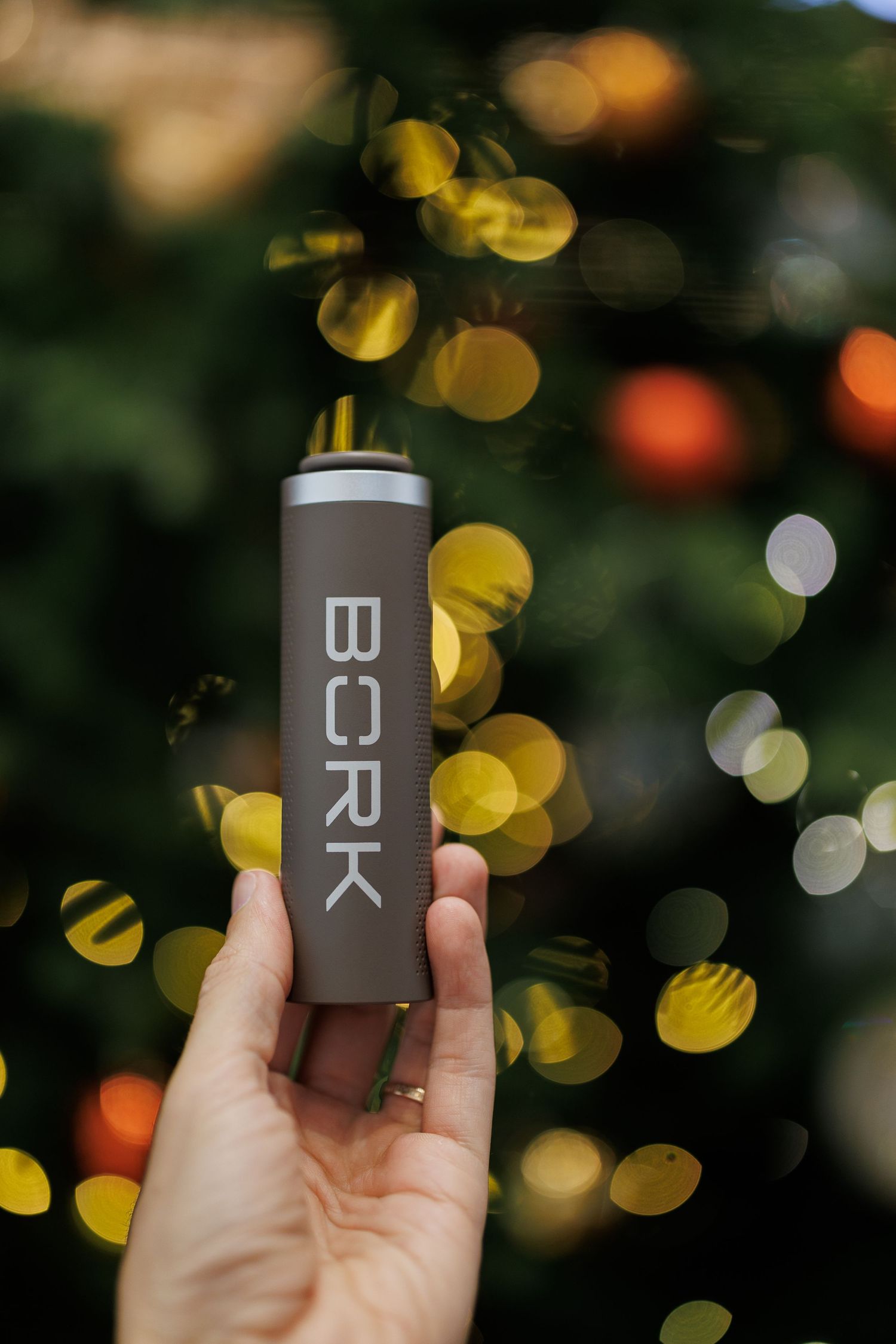 Hand holding dark minimalist product packaging with letters against blurred holiday lights.