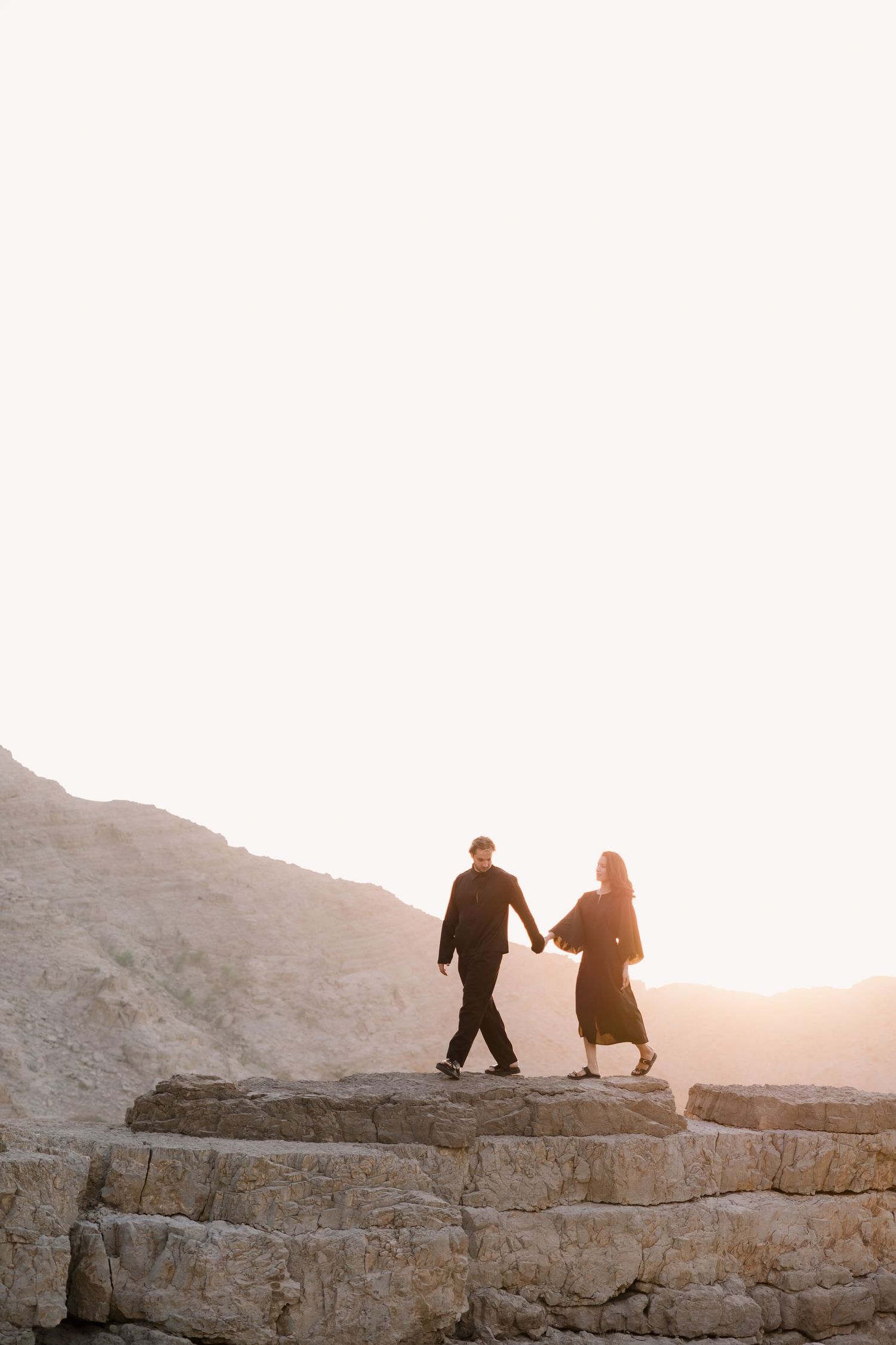 A couple walking together on rocky terrain during sunset in a desert setting.