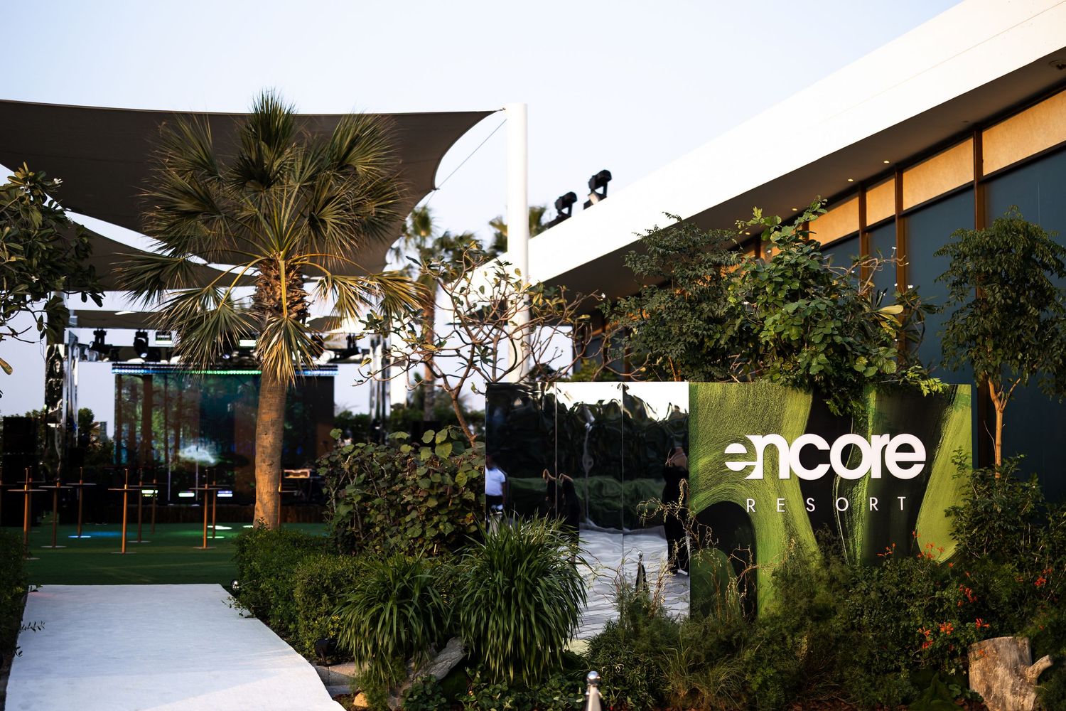 Modern outdoor resort walkway surrounded by lush tropical landscaping and palm trees illuminated at dusk.