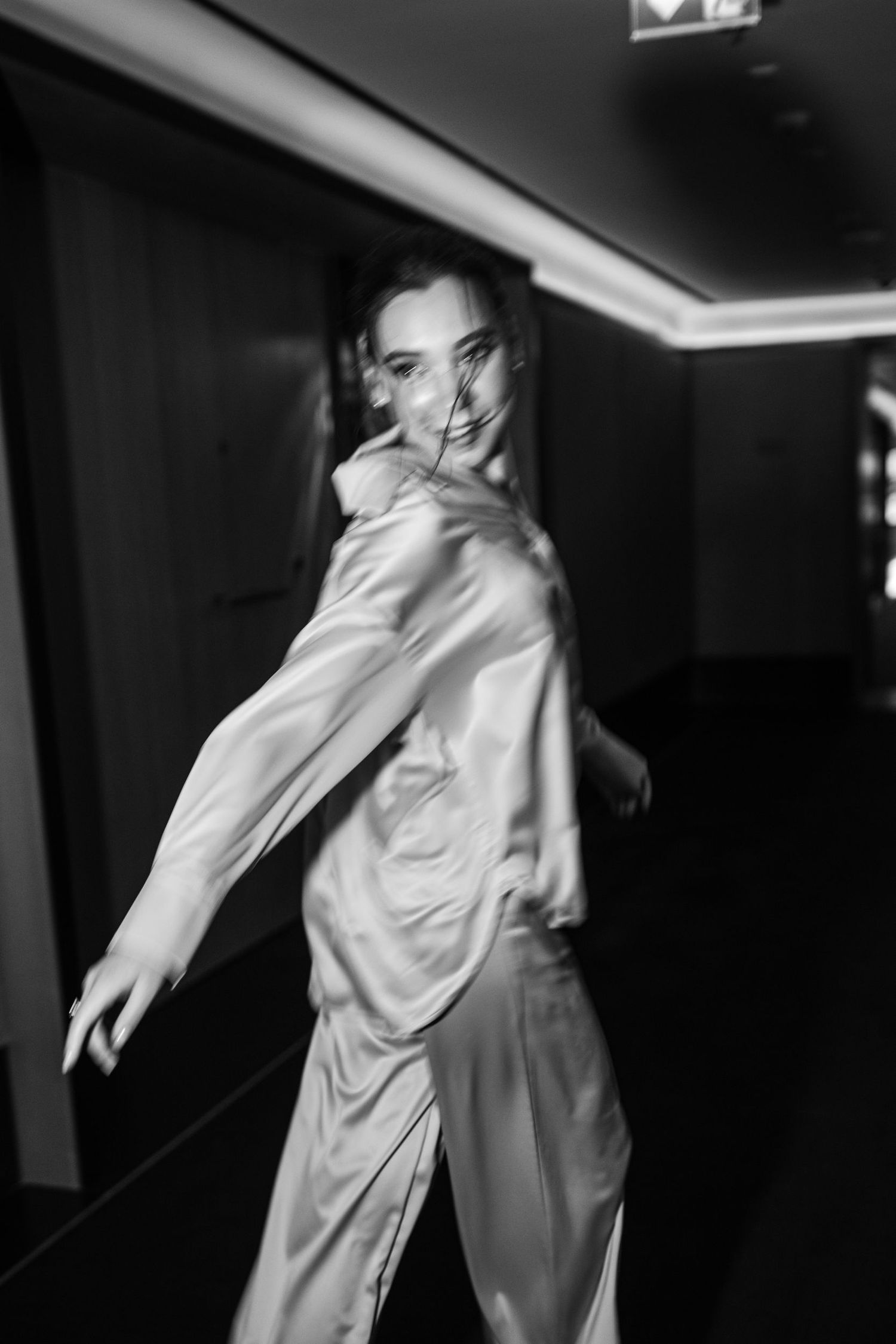 Motion shot of someone in silk pajamas twirling in a dark hallway.
