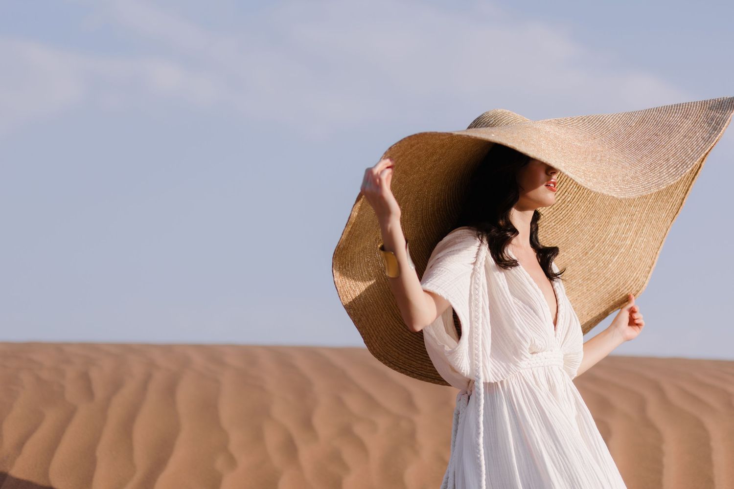 Figure in flowing white clothing walking across desert sand dunes.