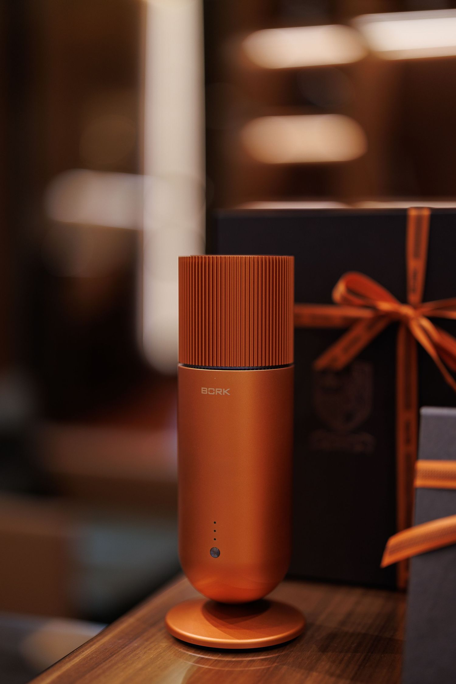 Orange cylindrical BORK product displayed with ribbon against blurred background.