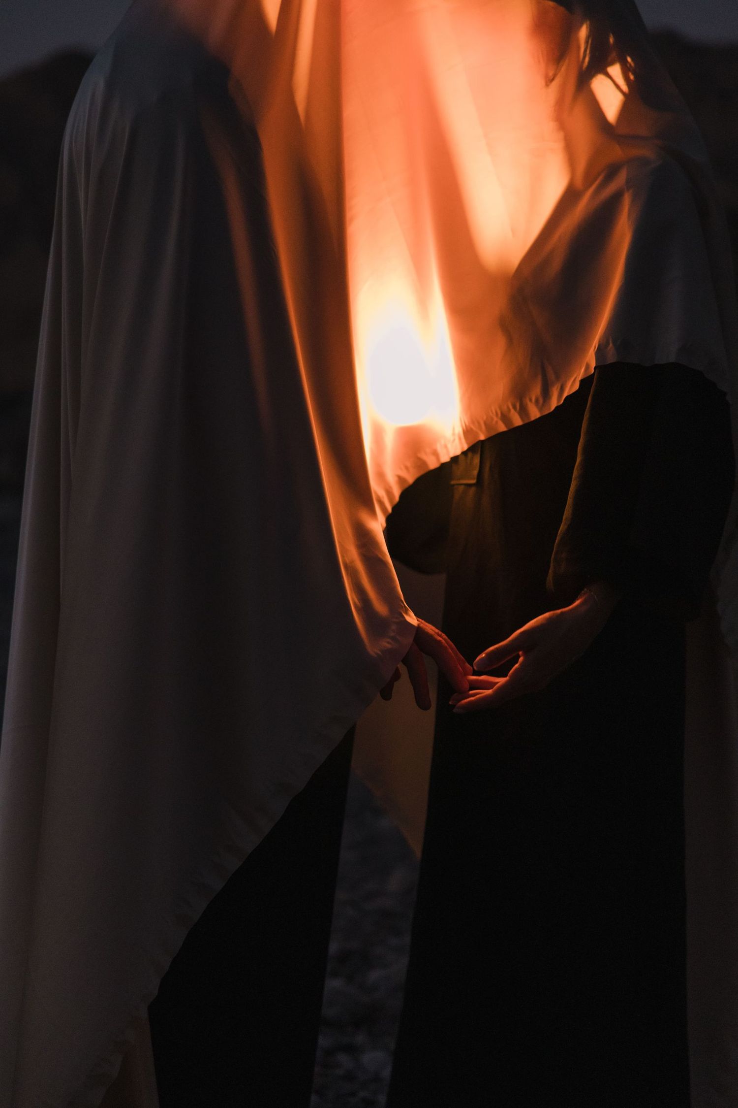 Orange fabric illuminated from behind creates ethereal flowing shapes in darkness.